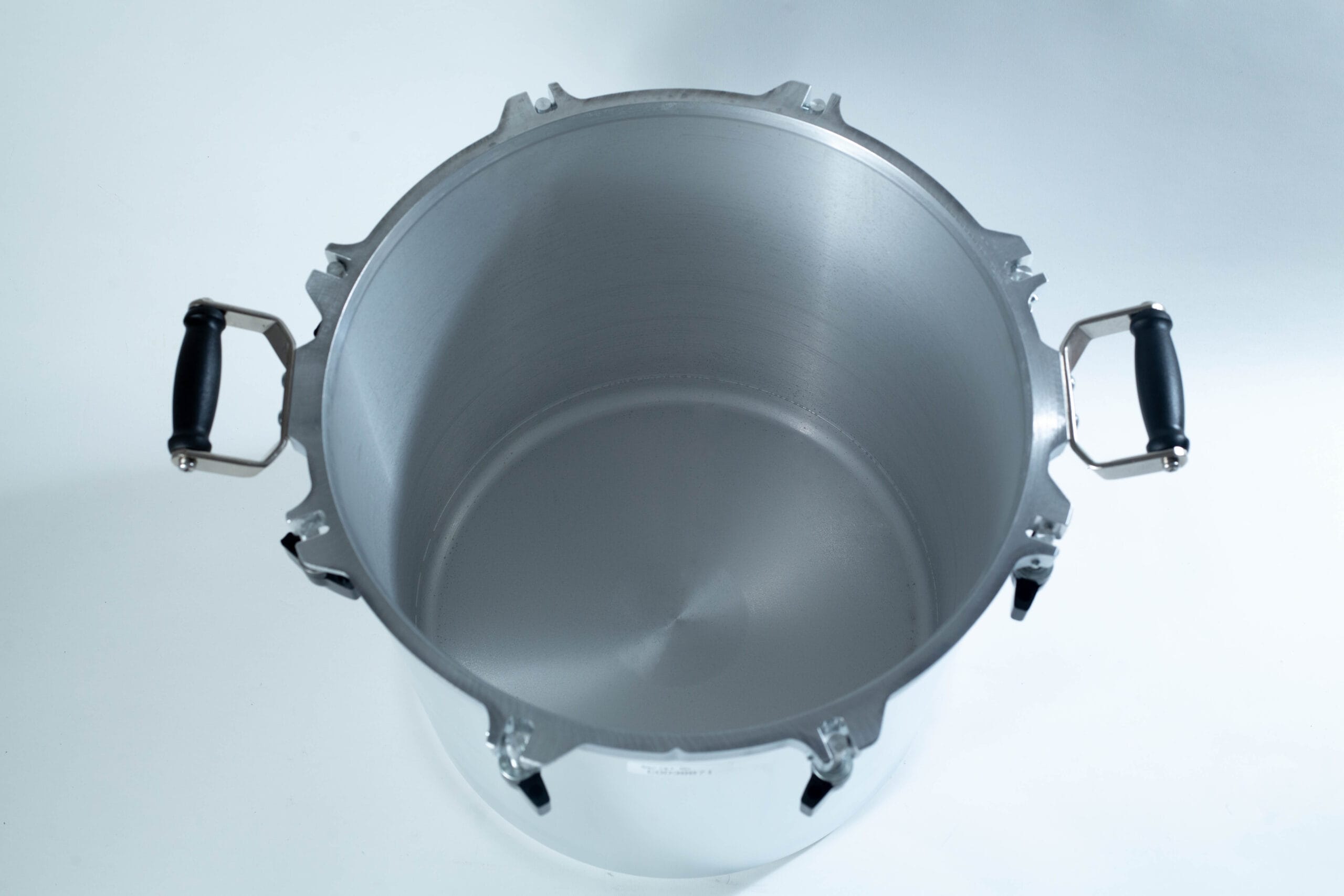 Top view of an empty stainless steel pressure cooker with black handles on a white surface.