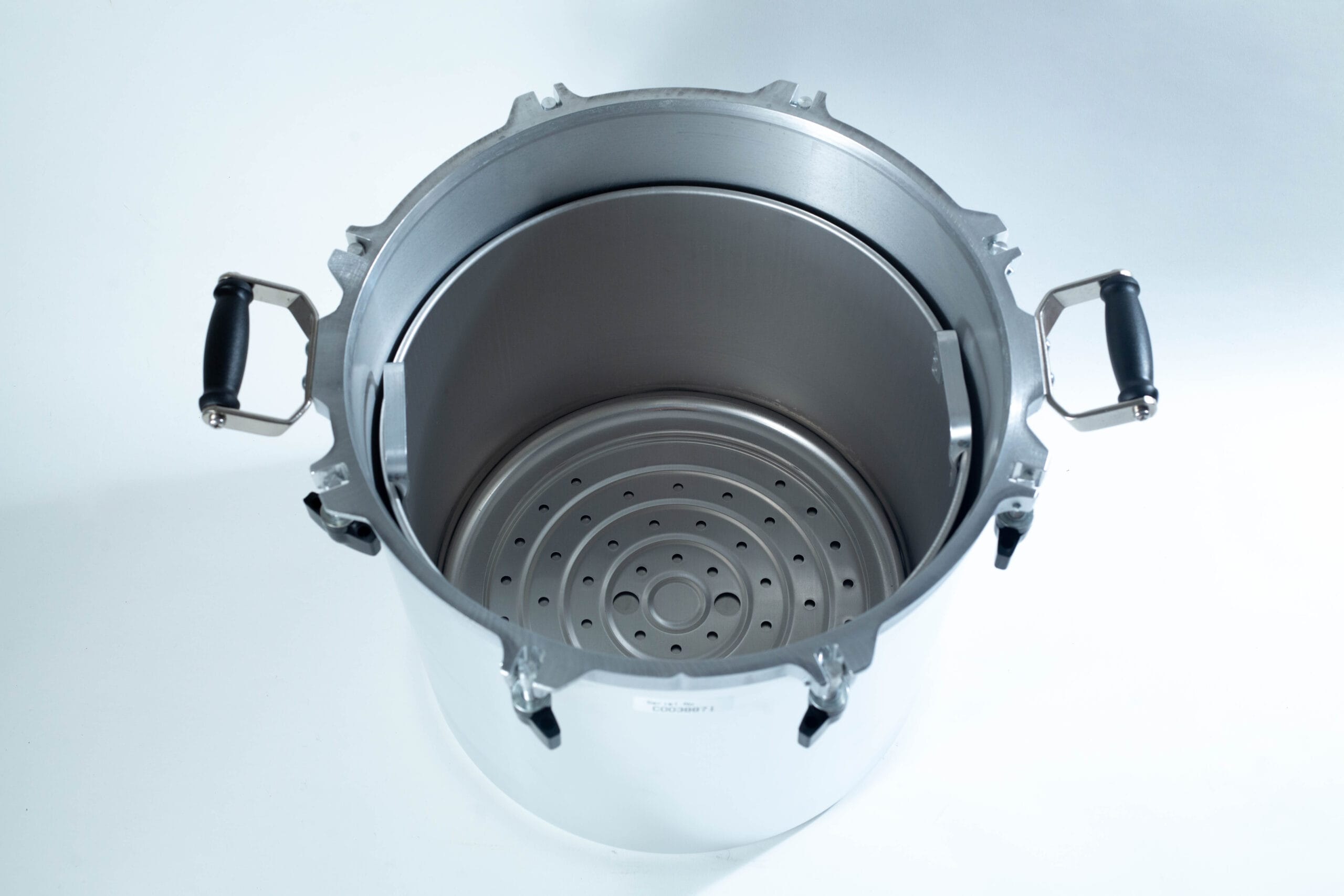 Top view of a large stainless steel pressure cooker with black handles and a perforated metal rack inside.