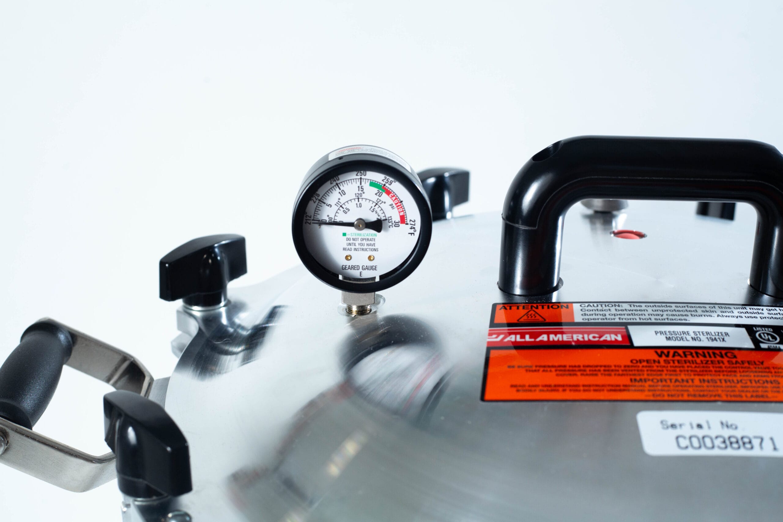 Close-up of the All American Wingnut pressure canner lid featuring a pressure gauge, handles, and warning labels.
