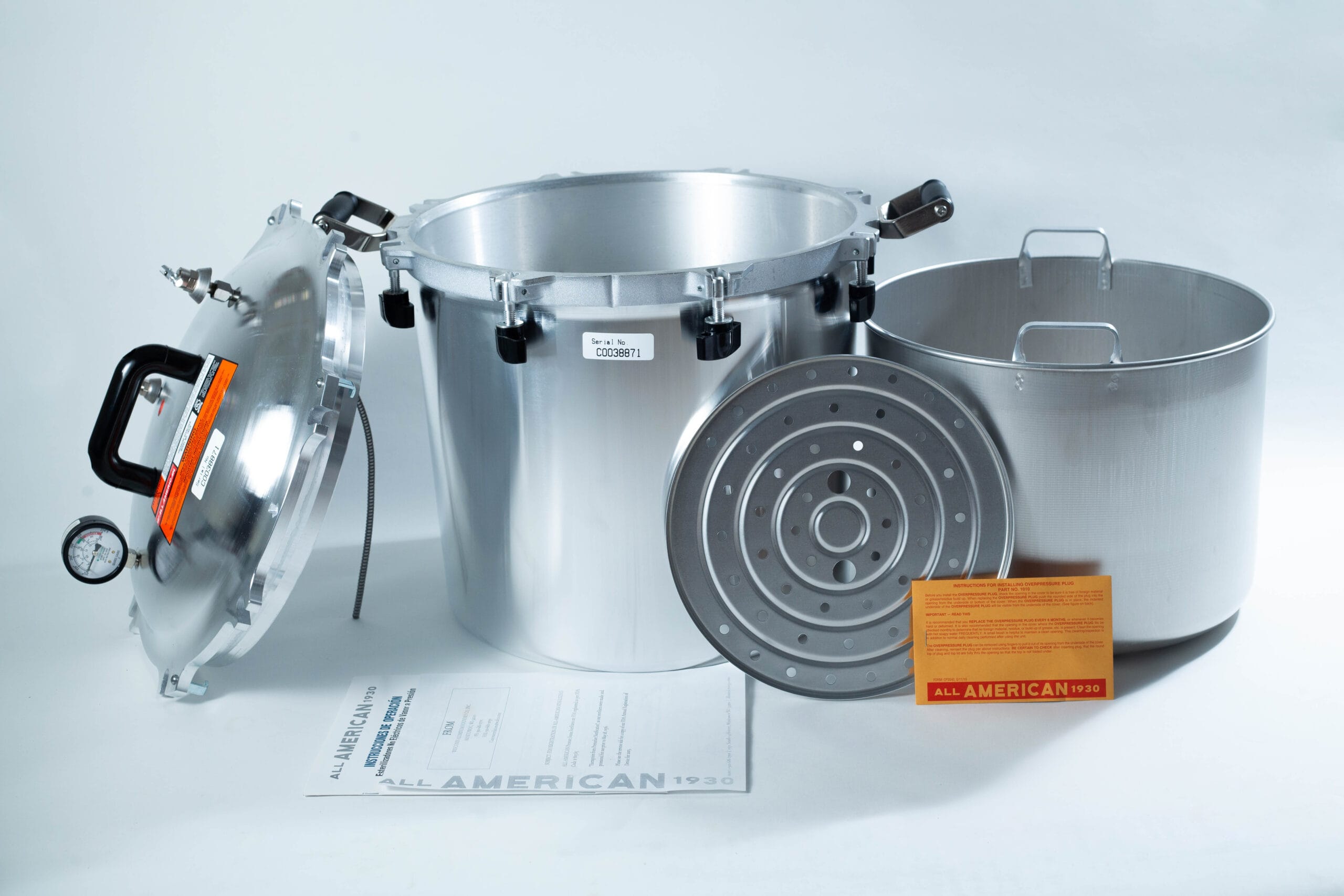 All American pressure cooker with lid, inner pot, metal rack, instruction manual, and orange card displayed.