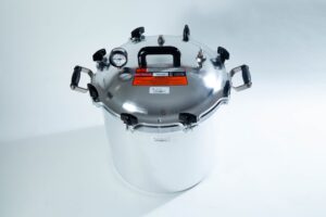 A large stainless steel pressure cooker with a black handle and pressure gauge on a white background.