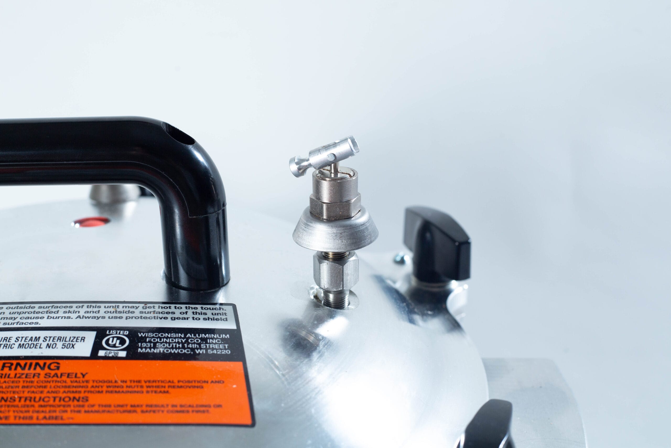Close-up of a pressure cooker lid showing the pressure release valve, handle, and warning label.