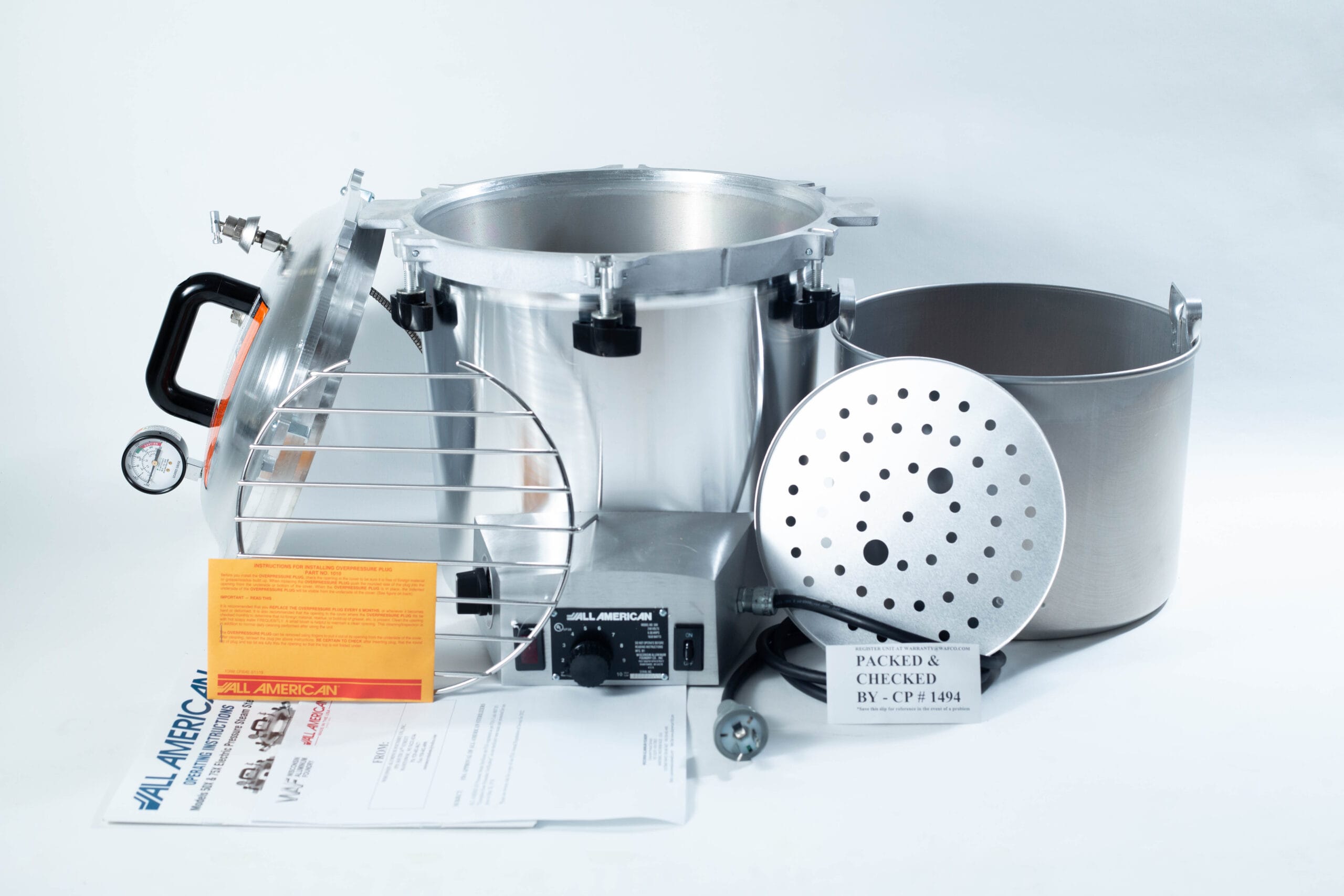 Parts of a pressure canner, including pot, lid, racks, gauge, and instruction leaflets, arranged on a white background.