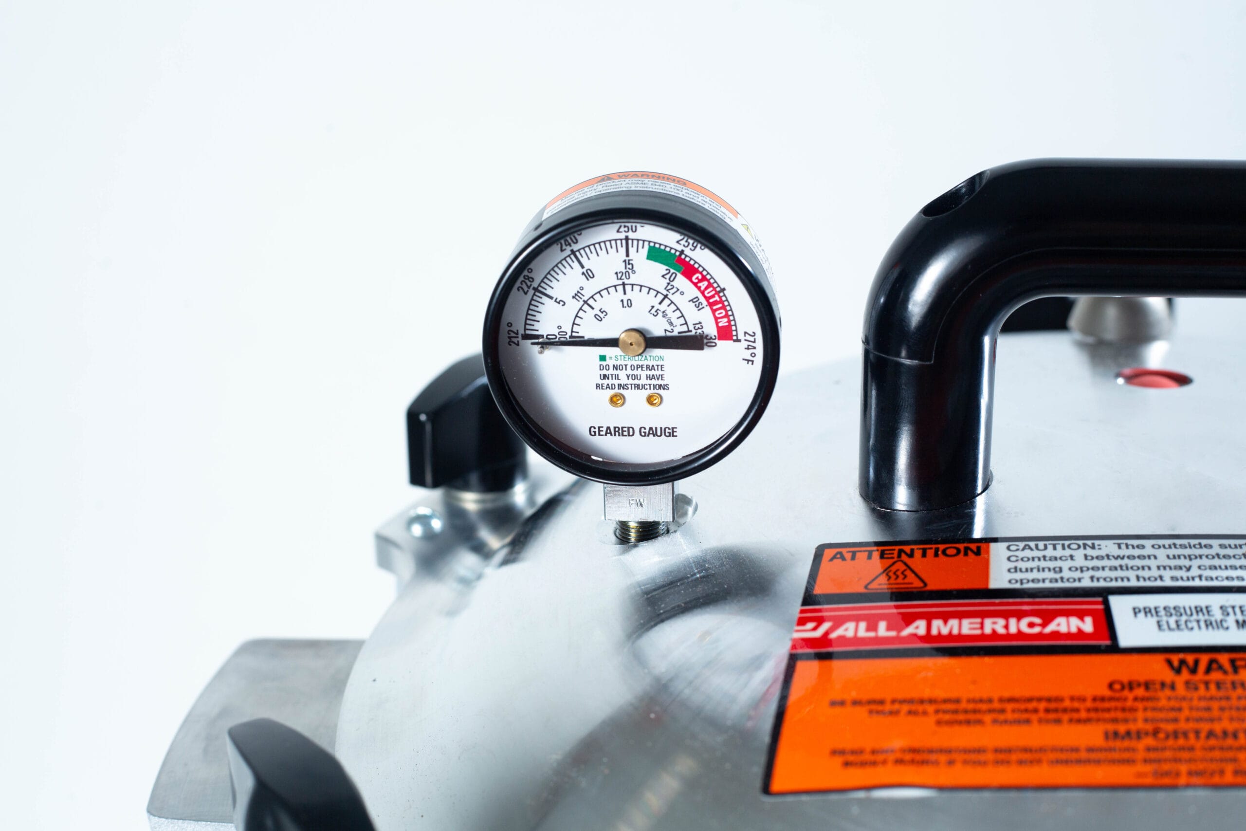 Close-up of a pressure gauge on a metal appliance with caution and warning labels visible.