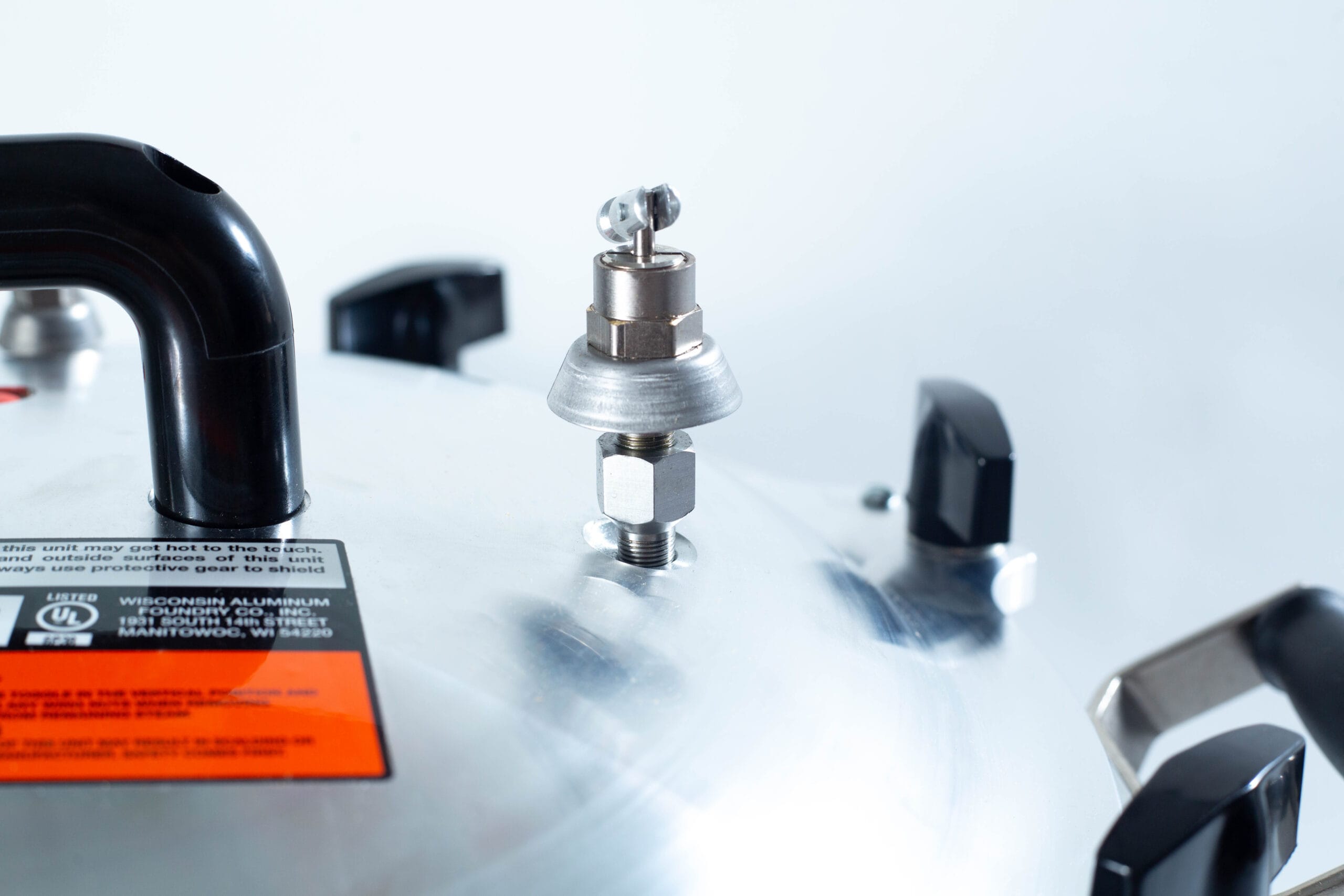 Close-up of a pressure cooker lid with a black handle and metal pressure release valve.