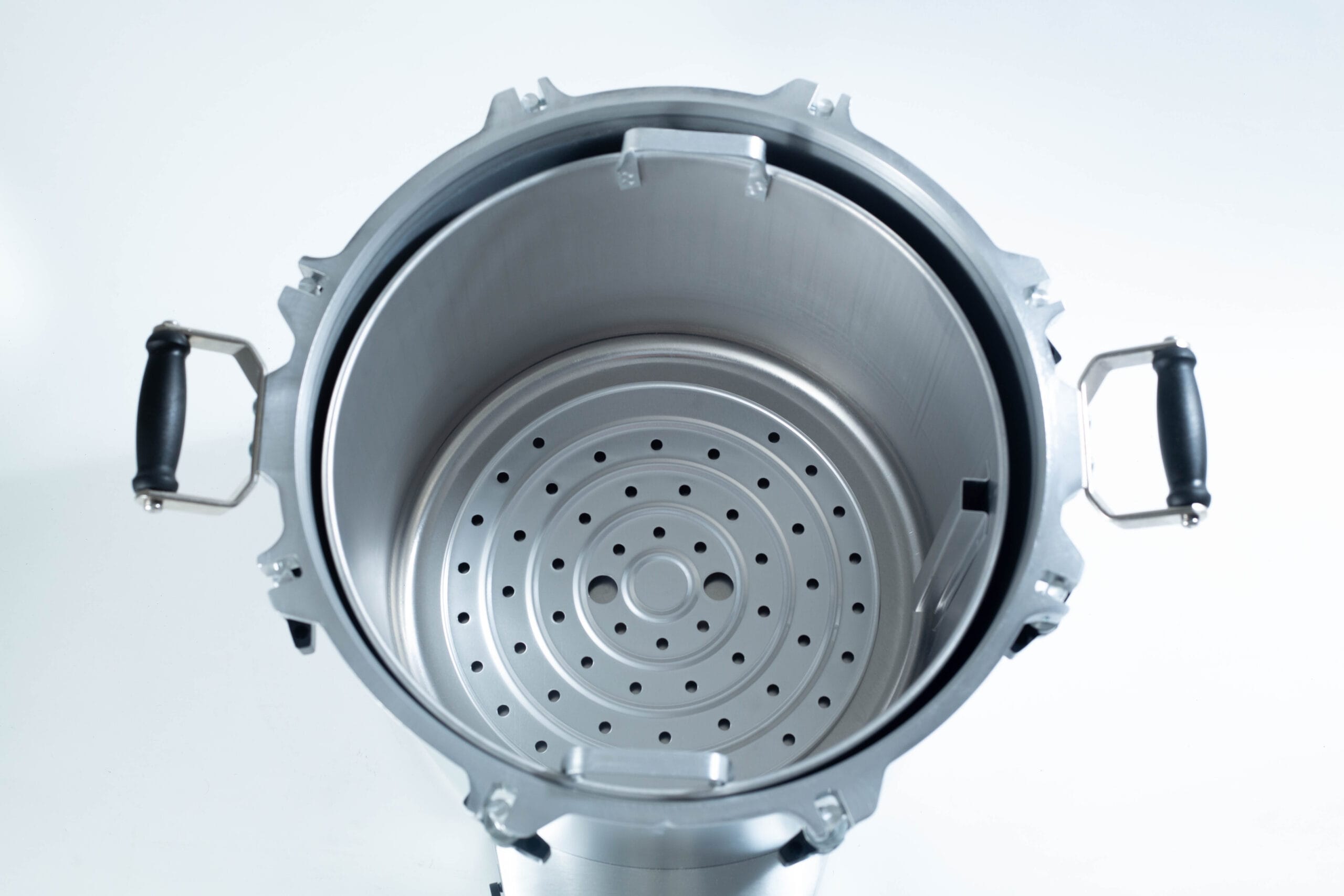 Top view of an empty stainless steel pressure cooker with black handles and a perforated steamer insert.