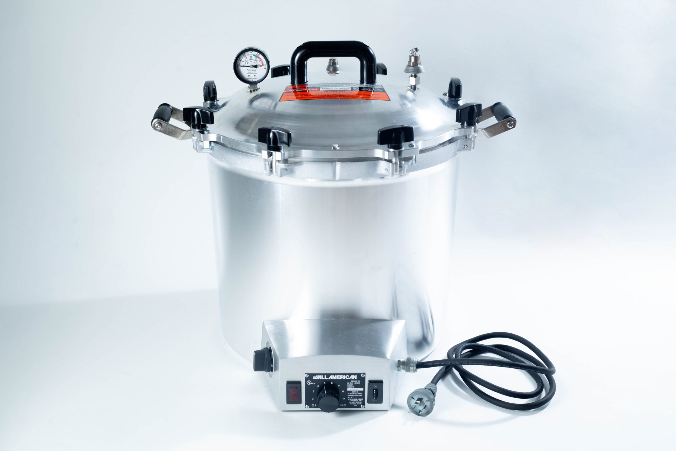 The All-American Wingnut is a large silver pressure cooker featuring gauge, latch handles, and a black power lead, shown on a white background.