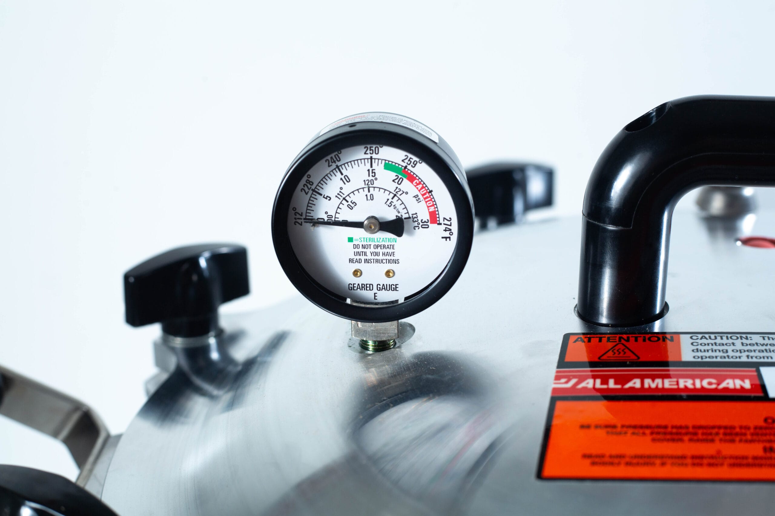 Close-up of a pressure gauge on a metal pressure cooker with caution labels visible.
