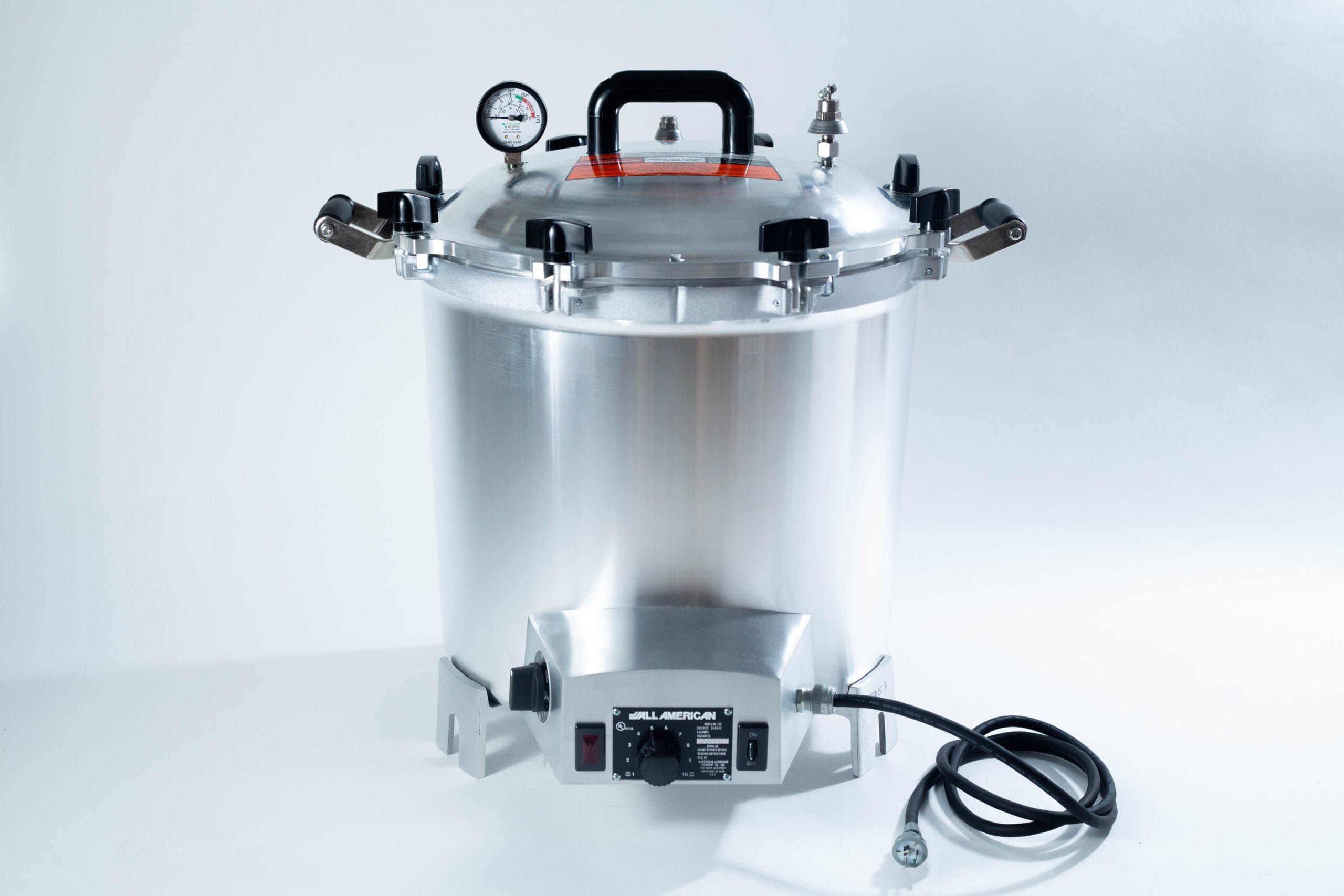 A stainless steel electric pressure cooker with a gauge, handle, and attached power lead.