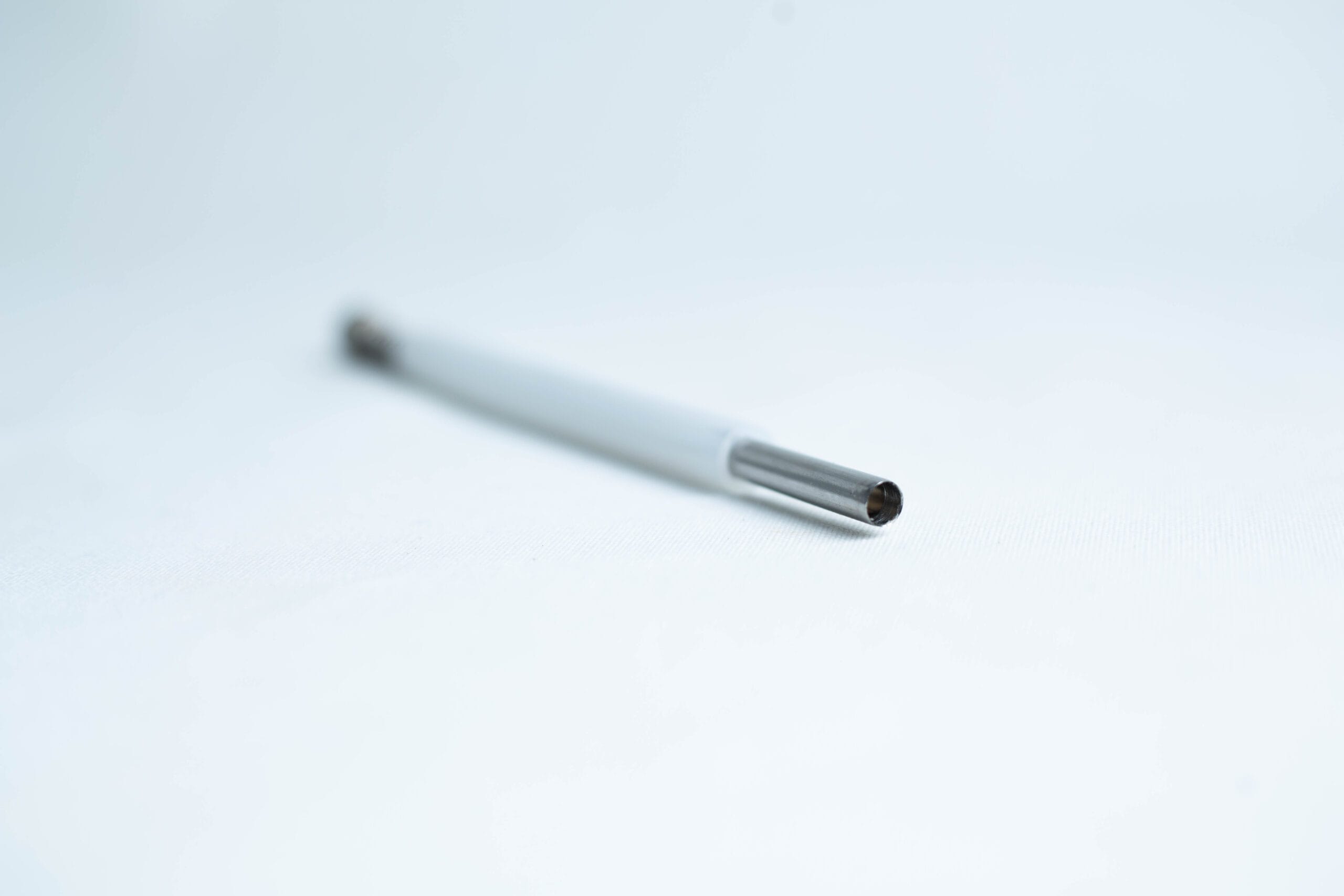 A close-up of a pen refill lying on a white surface with a blurred background.