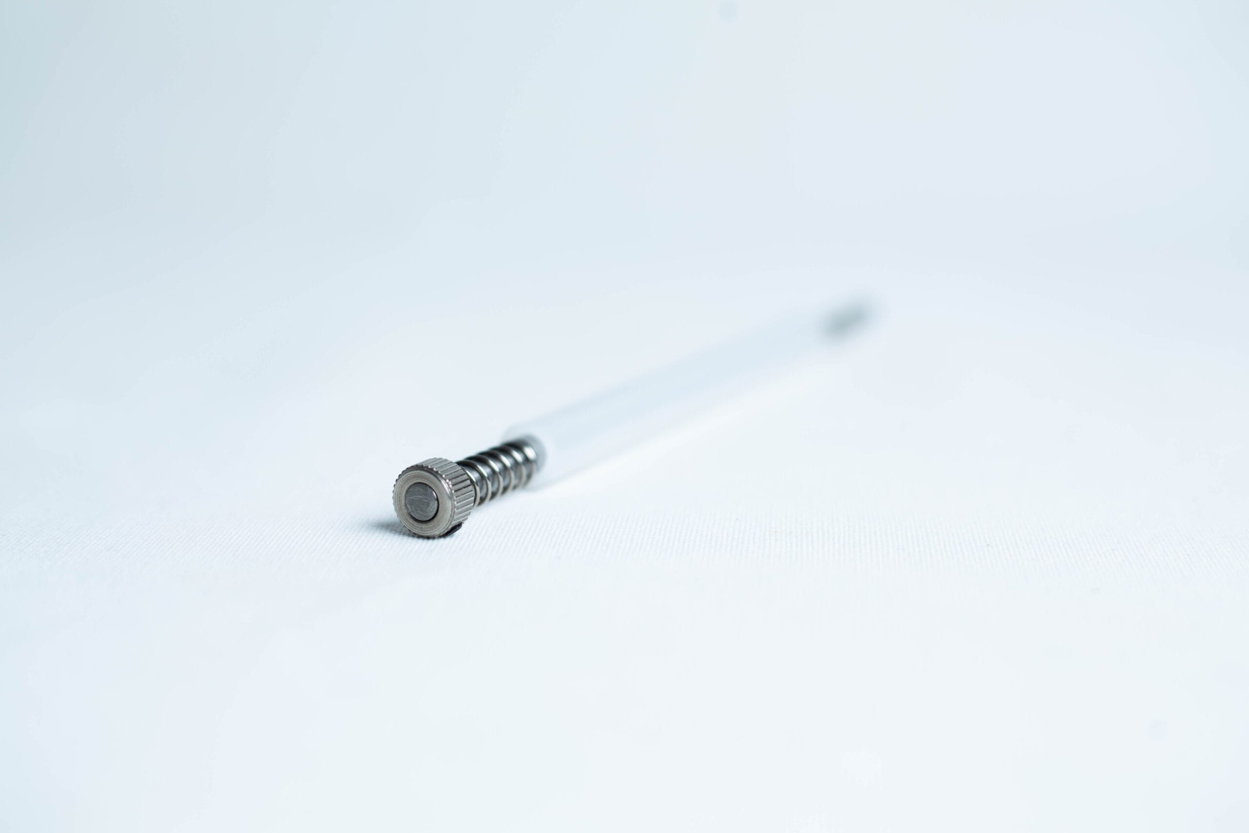 A metal spring pen refill lying on a white surface, photographed with a shallow depth of field.