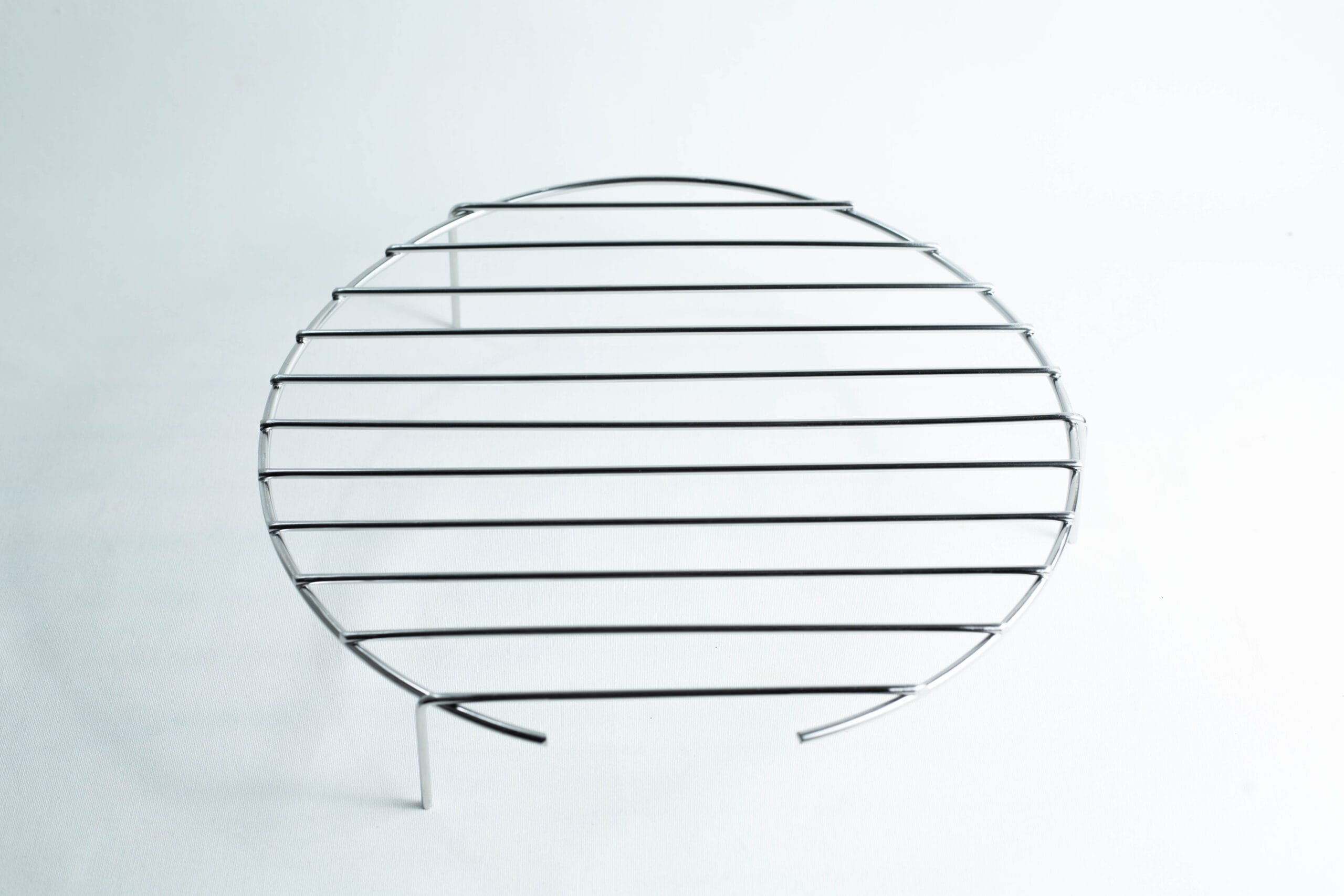 Round metal cooling rack with parallel bars and three short legs on a white background.