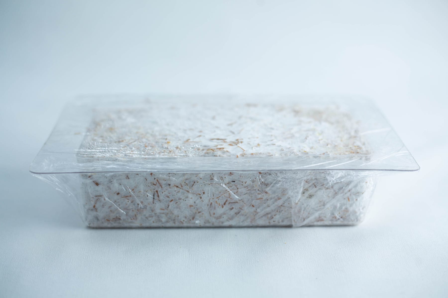 Rectangular container of white shredded material covered with clear plastic film against a plain background.