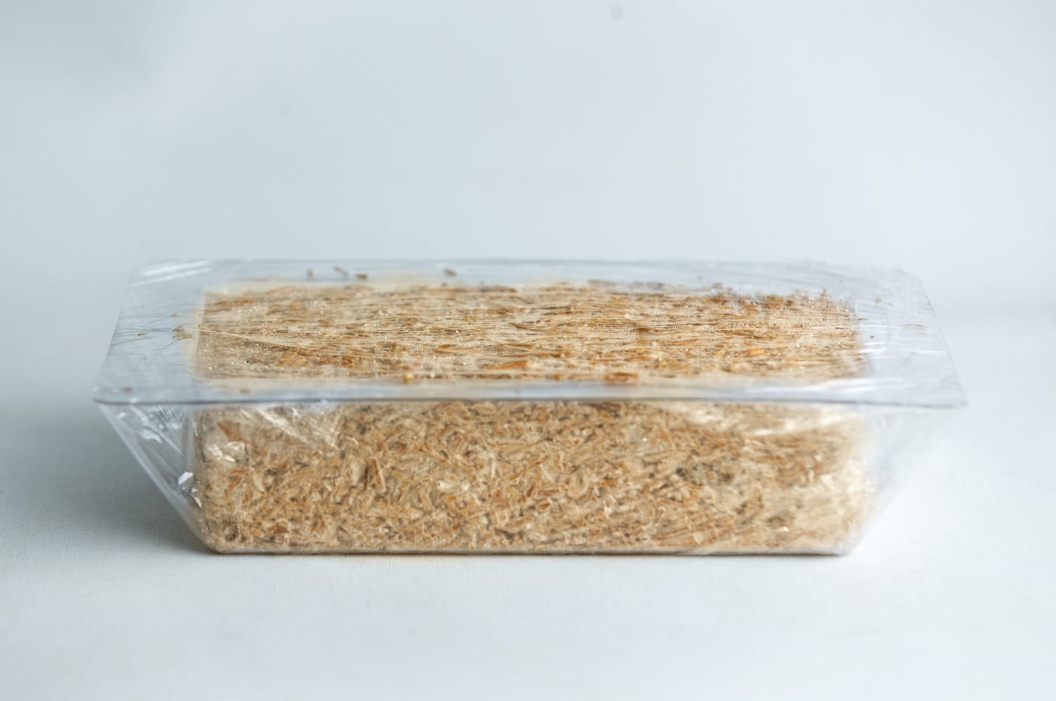A block of shredded wheat cereal in a clear plastic tray with a transparent wrapper.