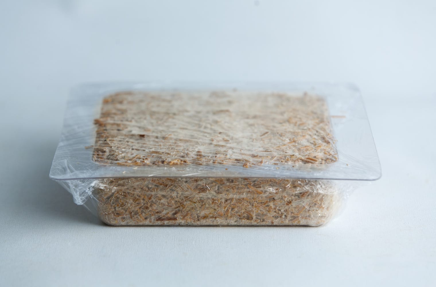 A rectangular block of food wrapped in plastic on a white surface.