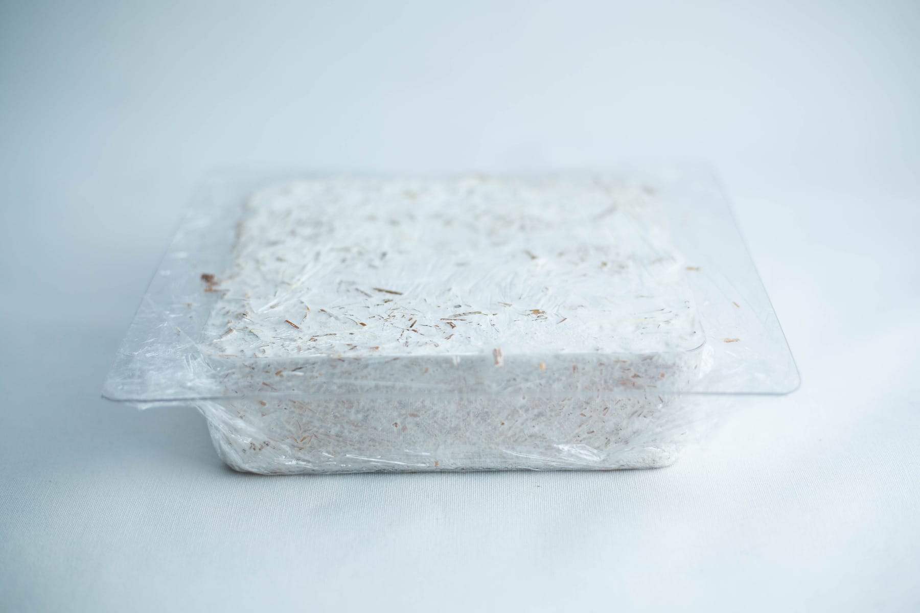 A block of white, shredded material in a clear plastic container on a light background.