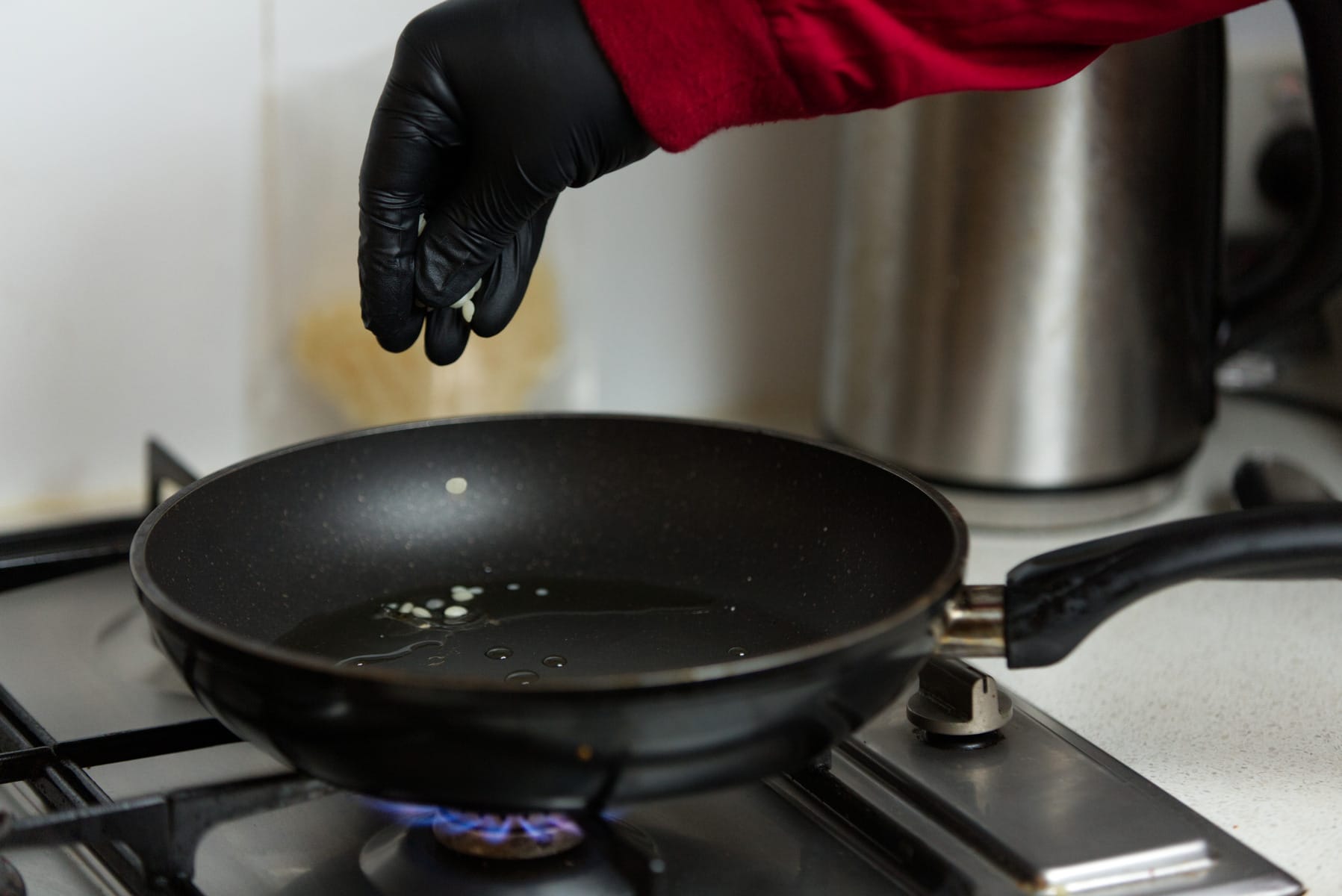 A gloved hand sprinkles ingredients from the Mushroom Log Kit | Mushroom Inoculation Kit (Sawdust Log) into a frying pan with oil on a lit gas hob.