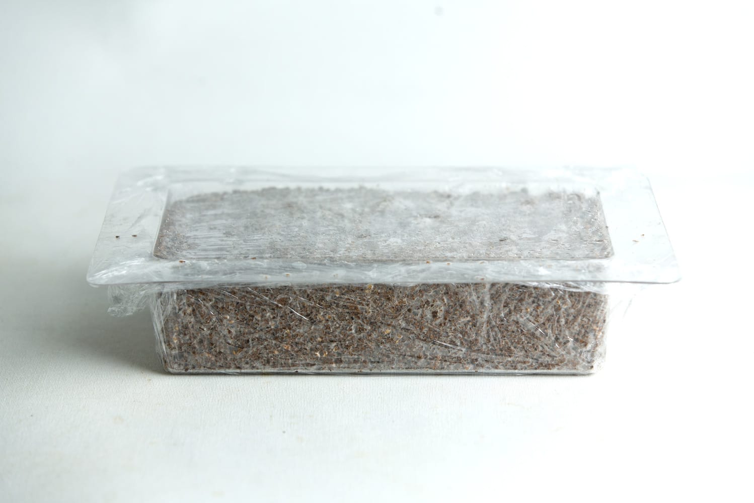 A rectangular plastic container filled with soil, covered with clear cling film.