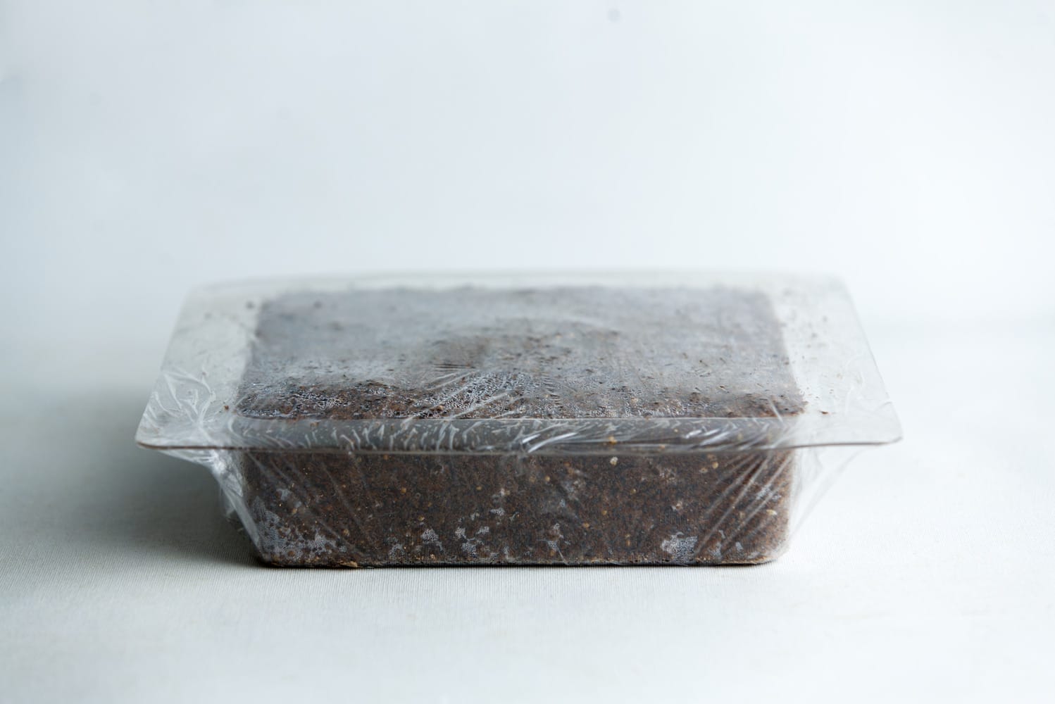 A rectangular block of soil in a plastic container covered with clear plastic film.