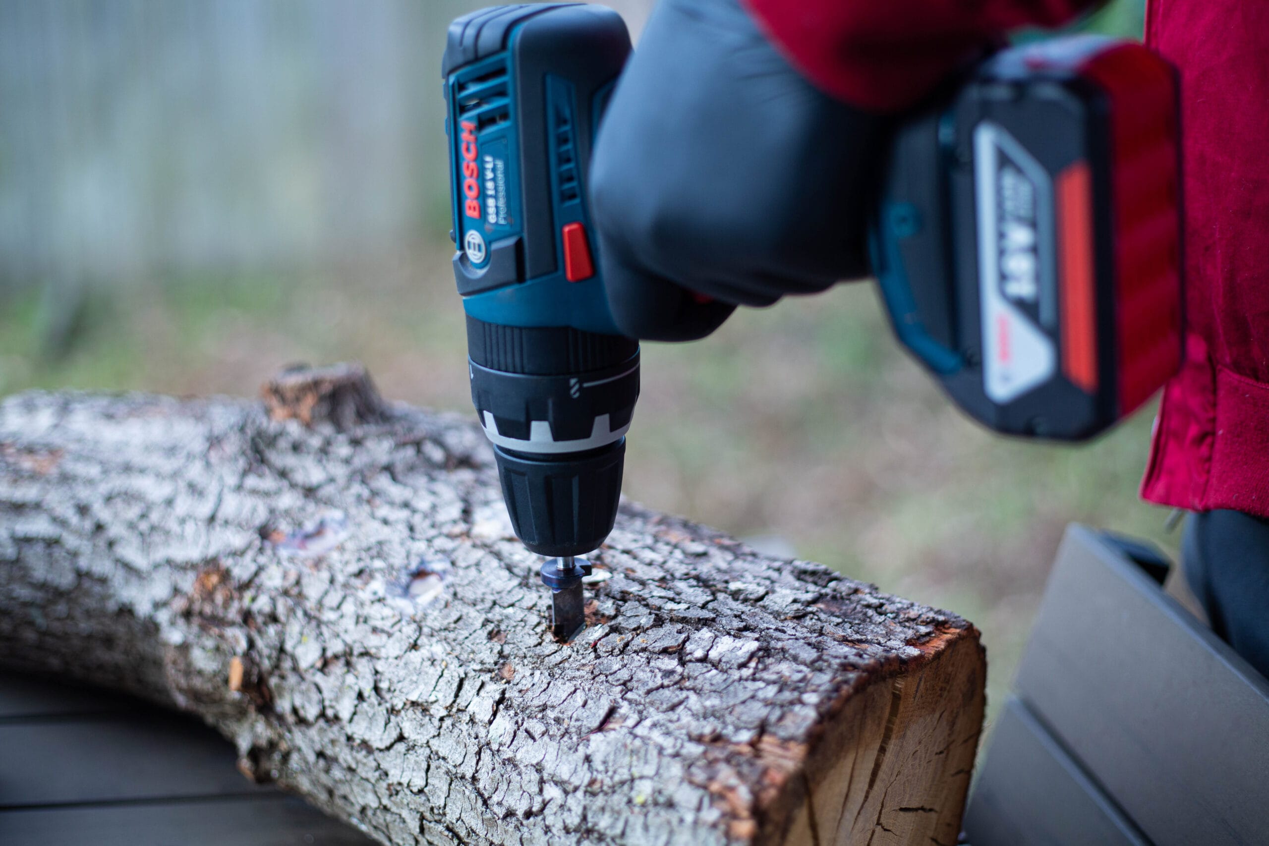 A person drills into a tree log using a cordless power drill outdoors.