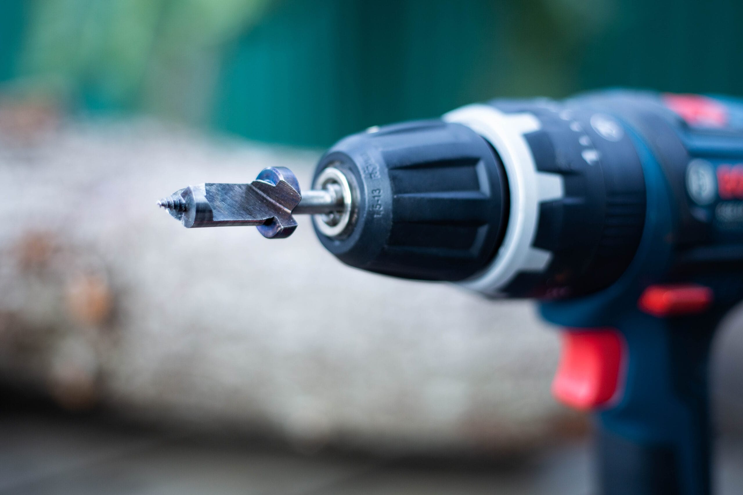 Close-up of a power drill with a drill bit attached, shown in an outdoor setting.