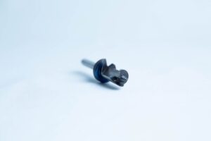 A close-up of a small black metal drill bit with a blue ring on a plain white background.