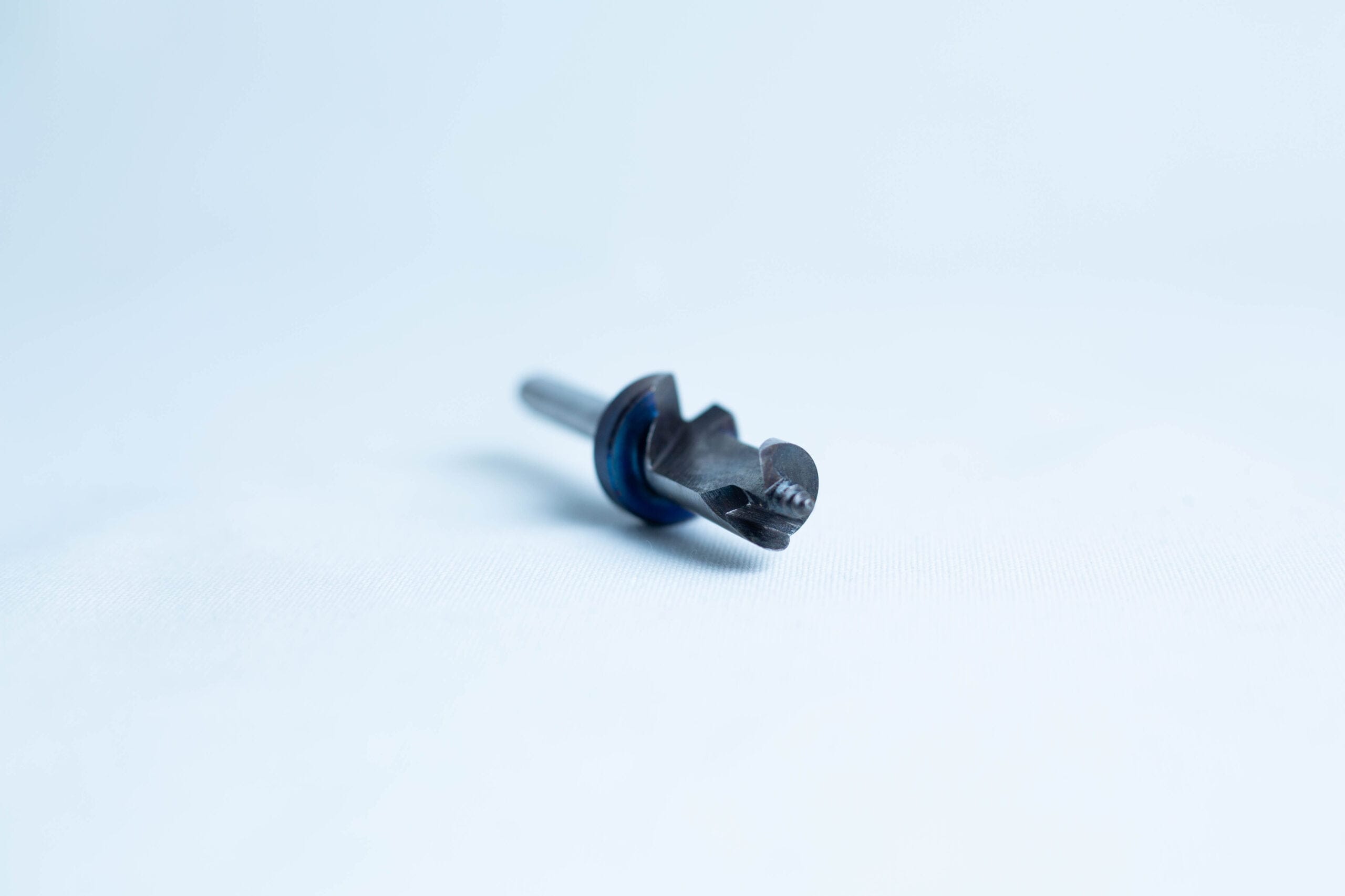 A close-up of a small black metal drill bit with a blue ring on a plain white background.