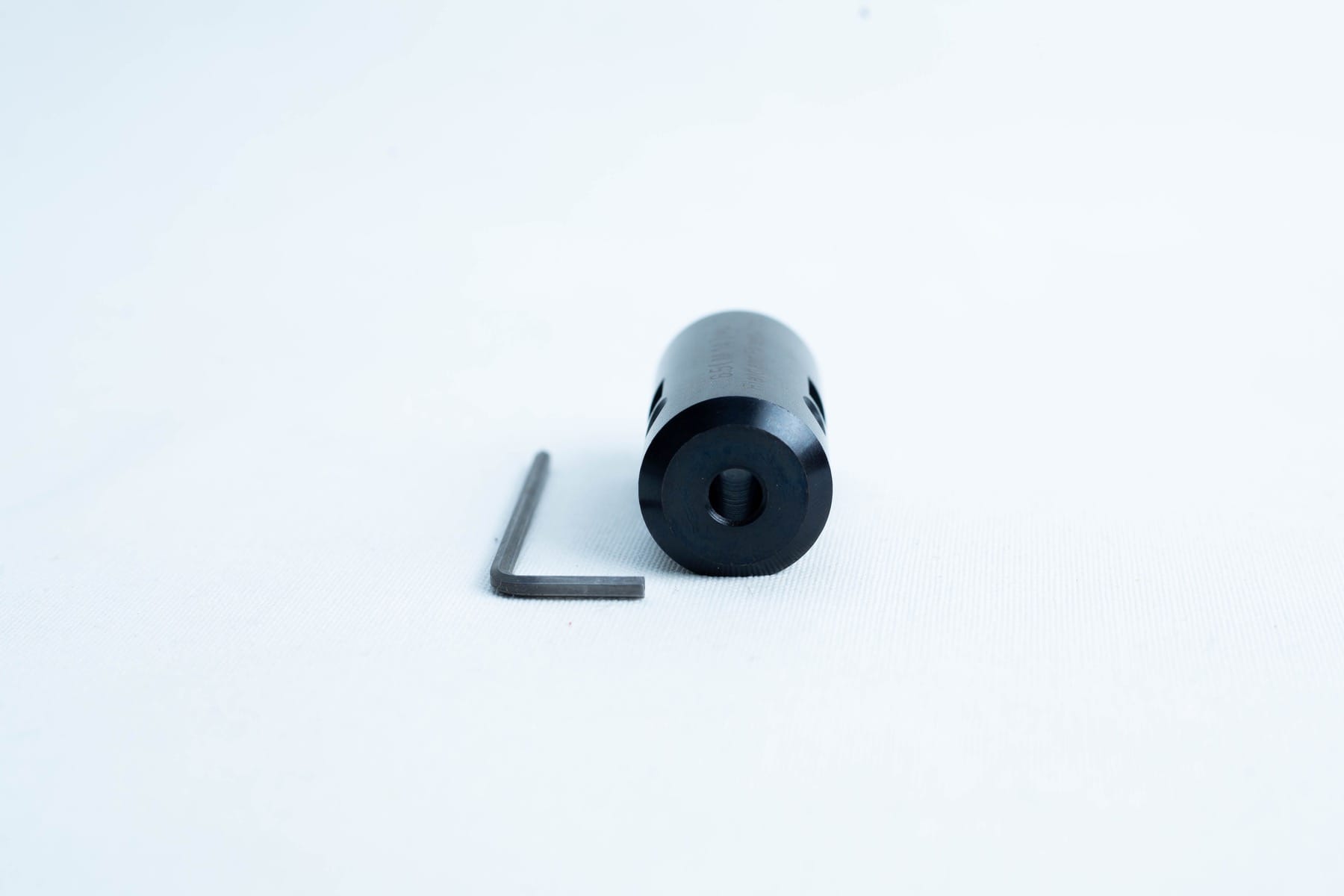 A black cylindrical metal part and an L-shaped hex key on a white background.