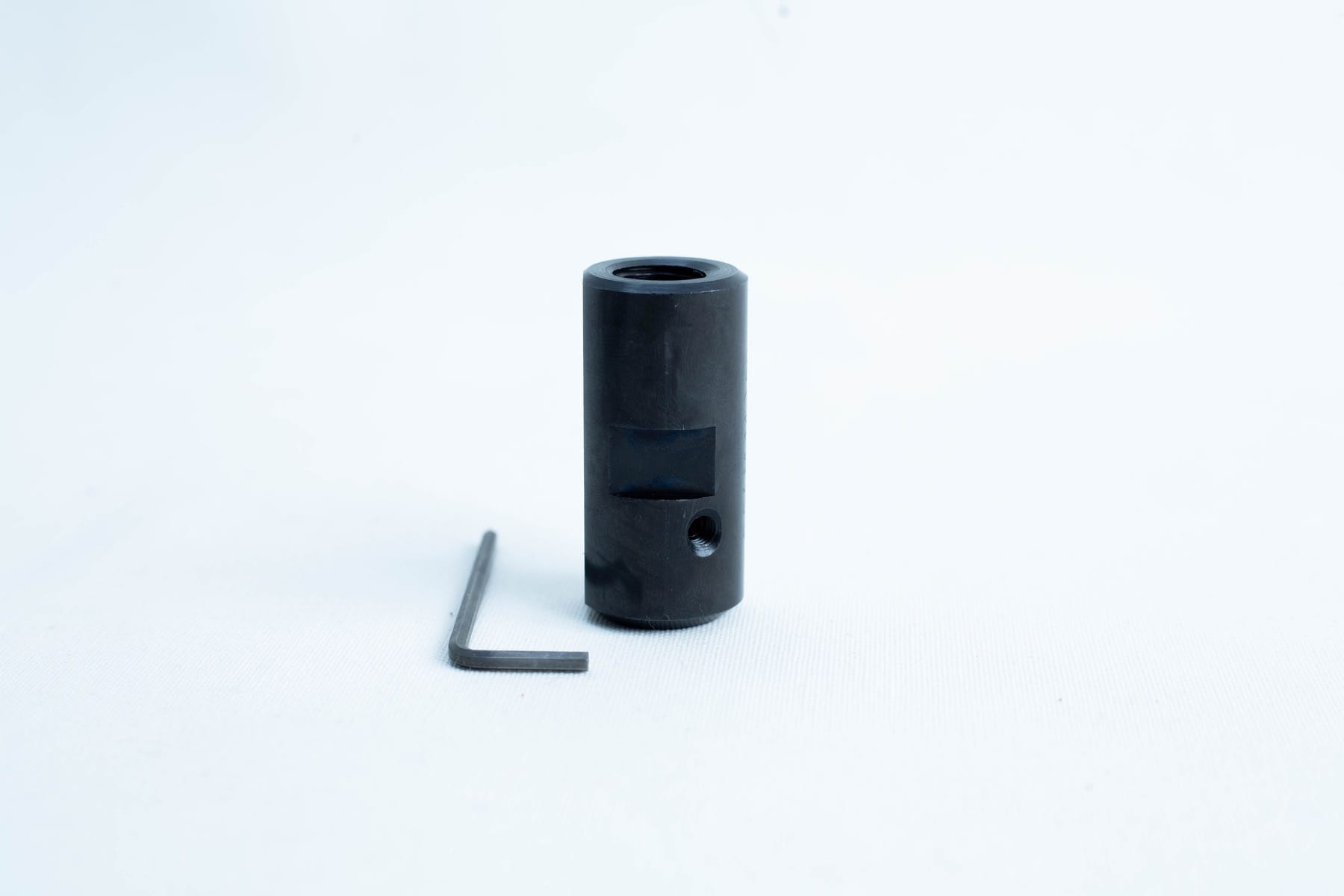 A black metal cylinder with a hole, next to a small L-shaped hex key on a white background.
