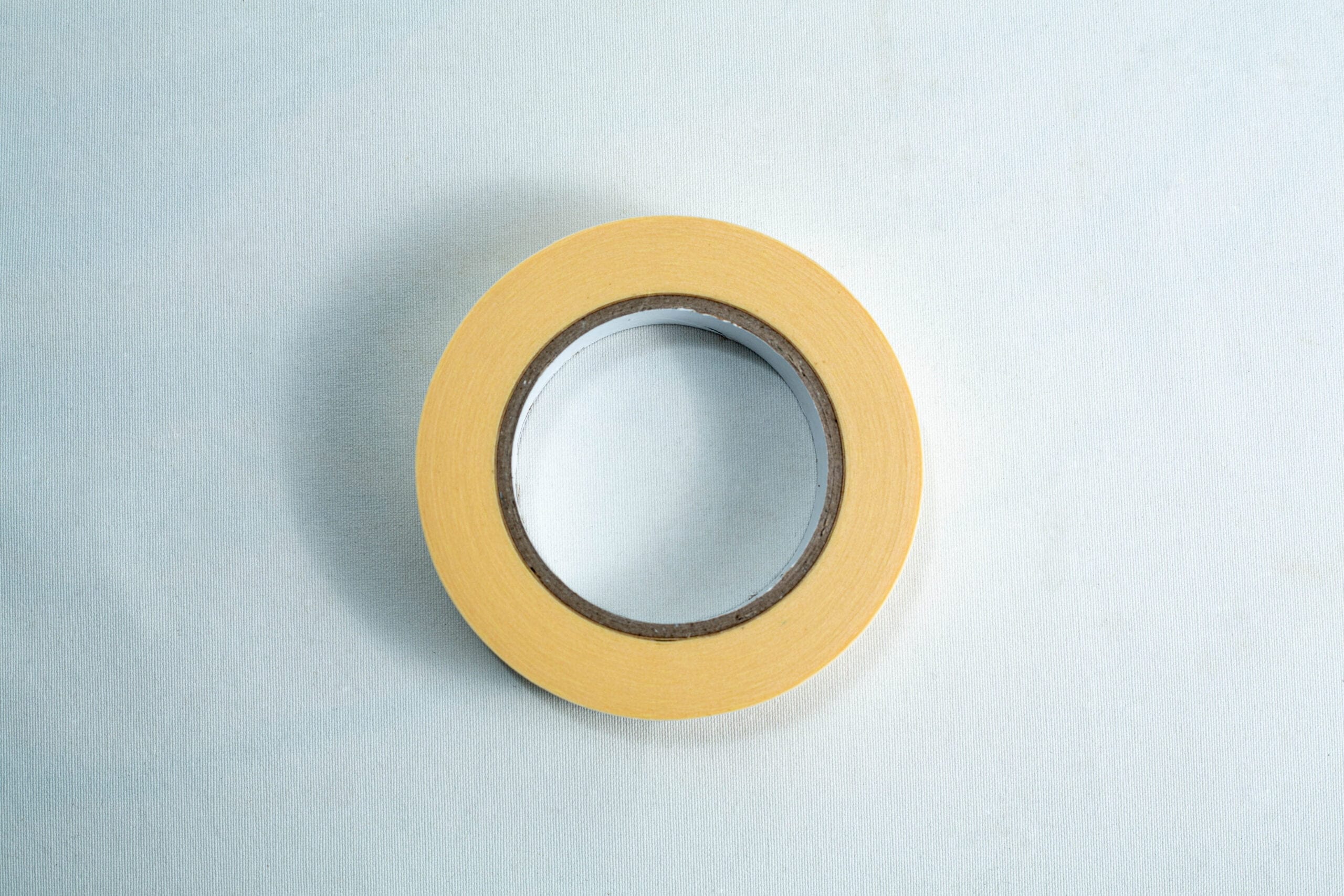 A roll of yellow masking tape on a light blue surface, viewed from above.