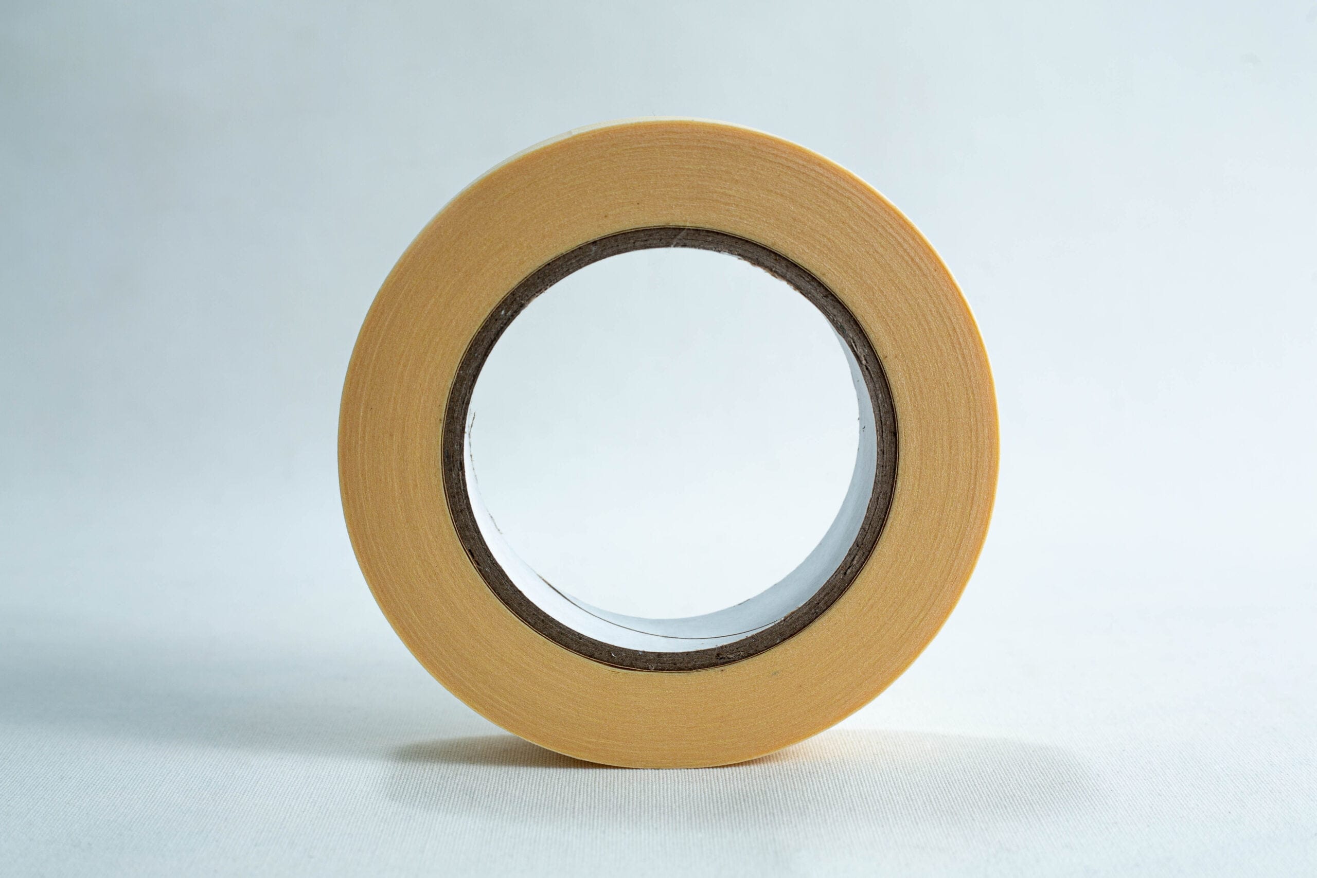 A roll of beige masking tape stands upright on a white surface against a light background.