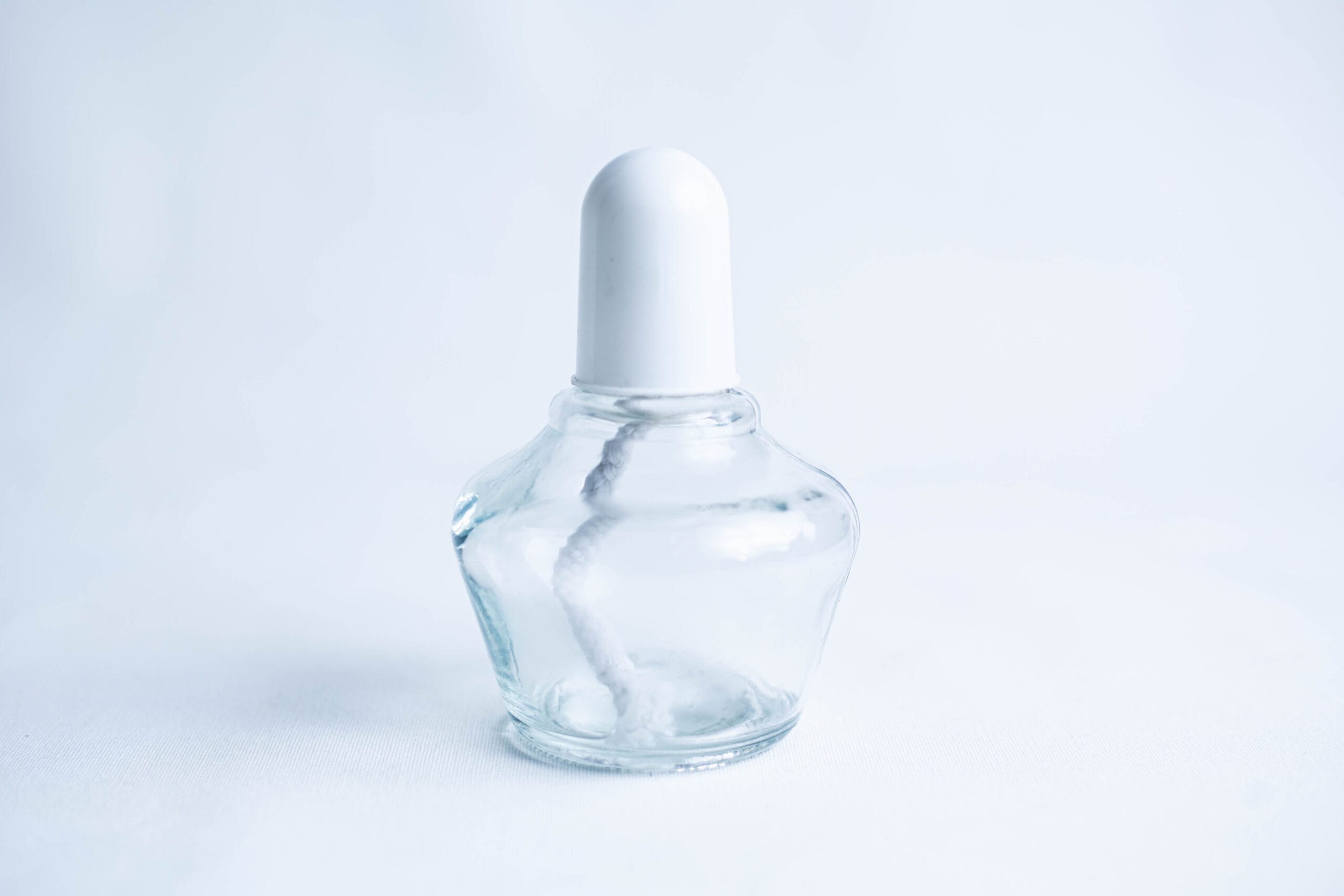 Clear glass bottle with a white cap and a visible cotton bud inside, set against a light background.