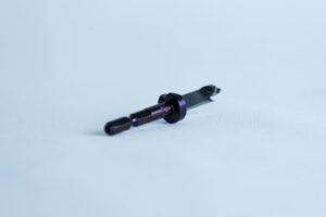 A small metallic tool with a cylindrical handle lies on a white surface, orientated diagonally.