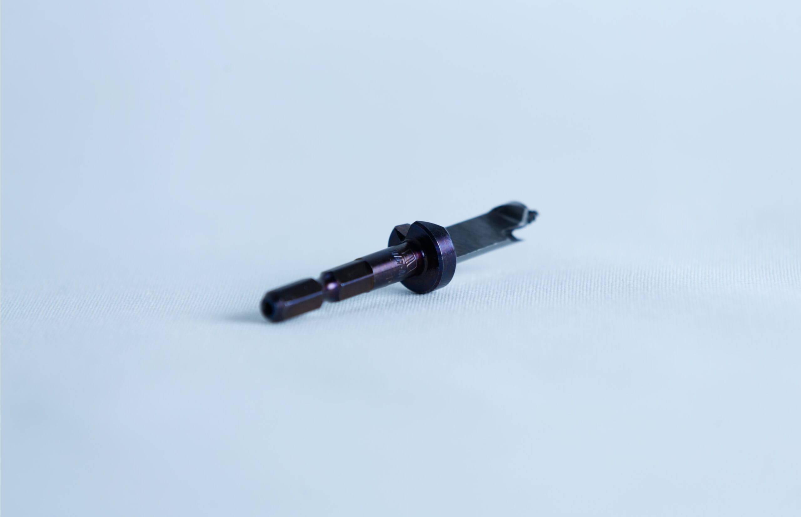 A small metallic tool with a cylindrical handle lies on a white surface, orientated diagonally.