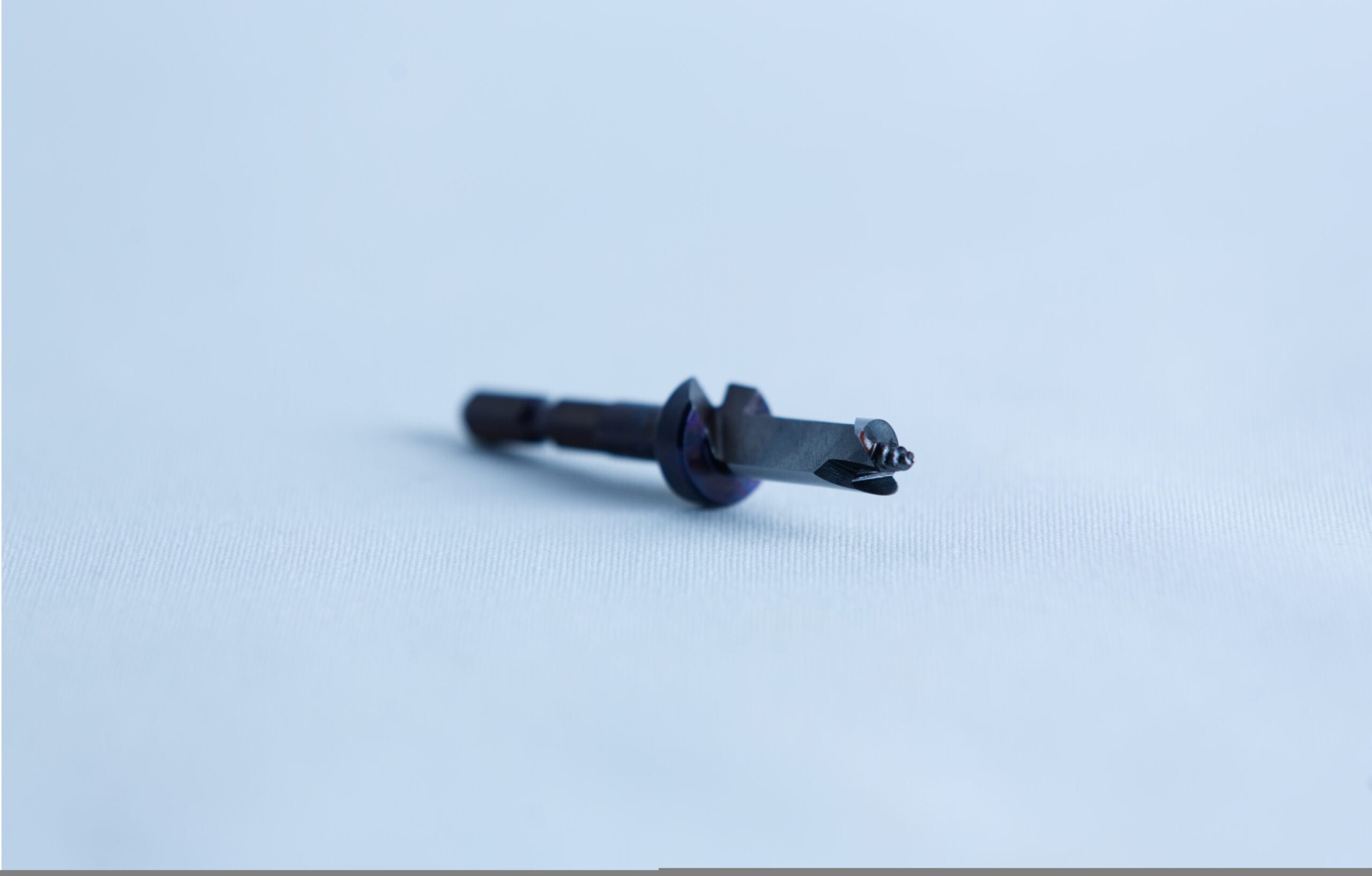 A close-up of a small metal tool or drill bit on a light blue surface with a blurred background.