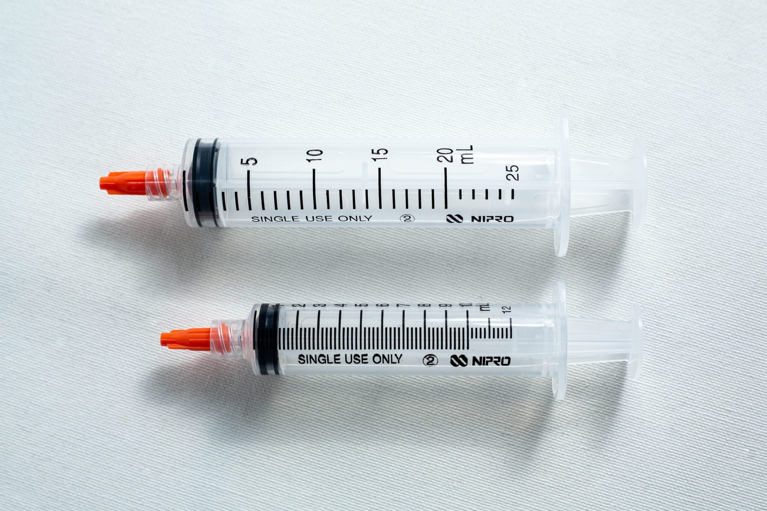 Two plastic syringes with orange caps lying side by side on a white surface.