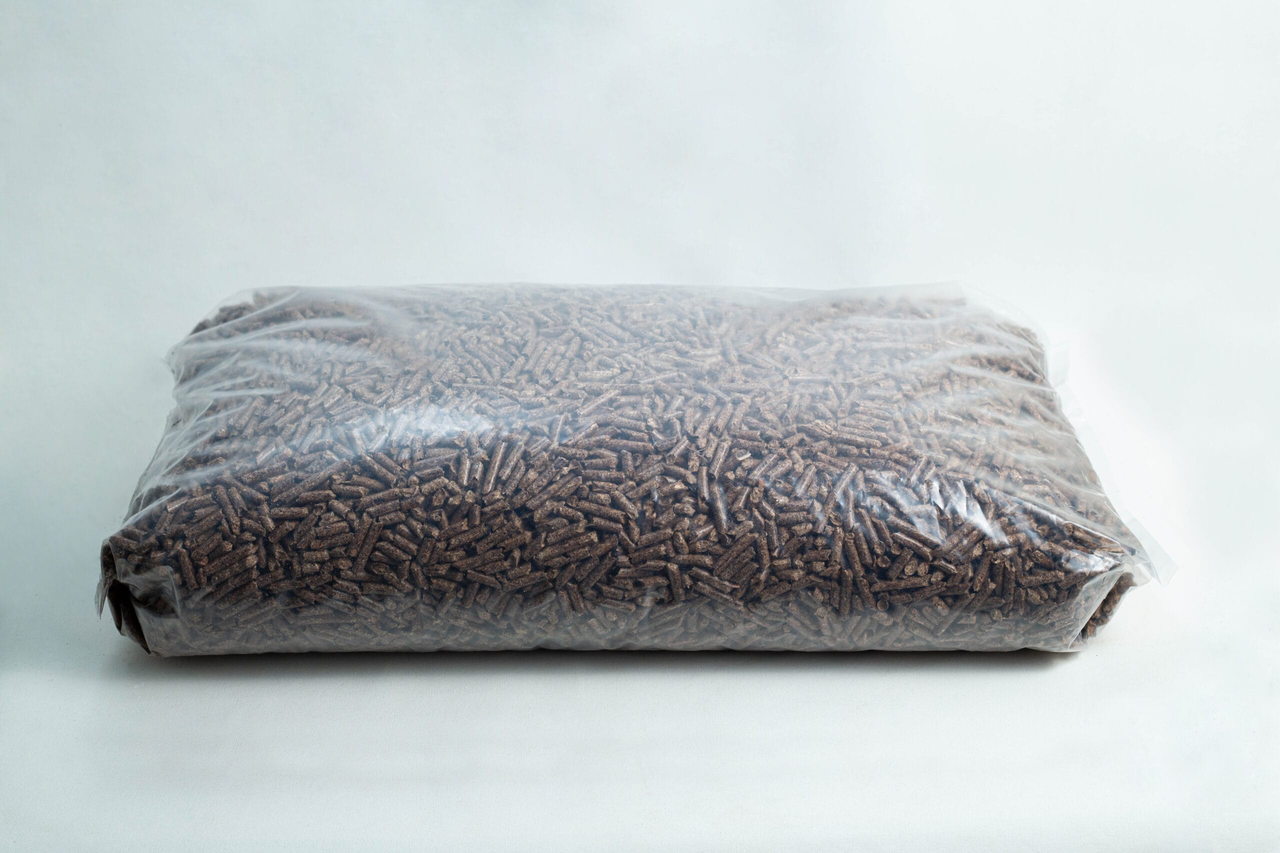 A sealed plastic bag filled with brown wood pellets on a plain white background.
