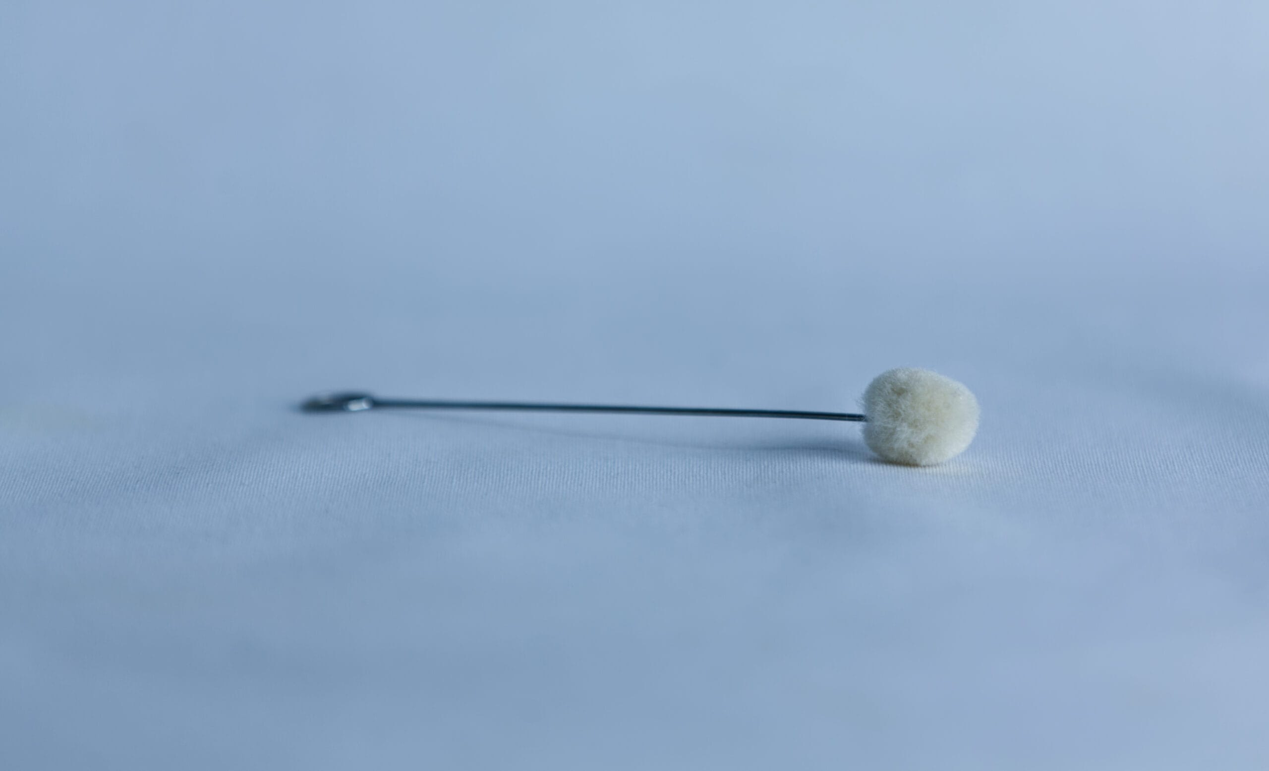 A single metal stick with a cotton bud lies on a smooth, light blue surface.