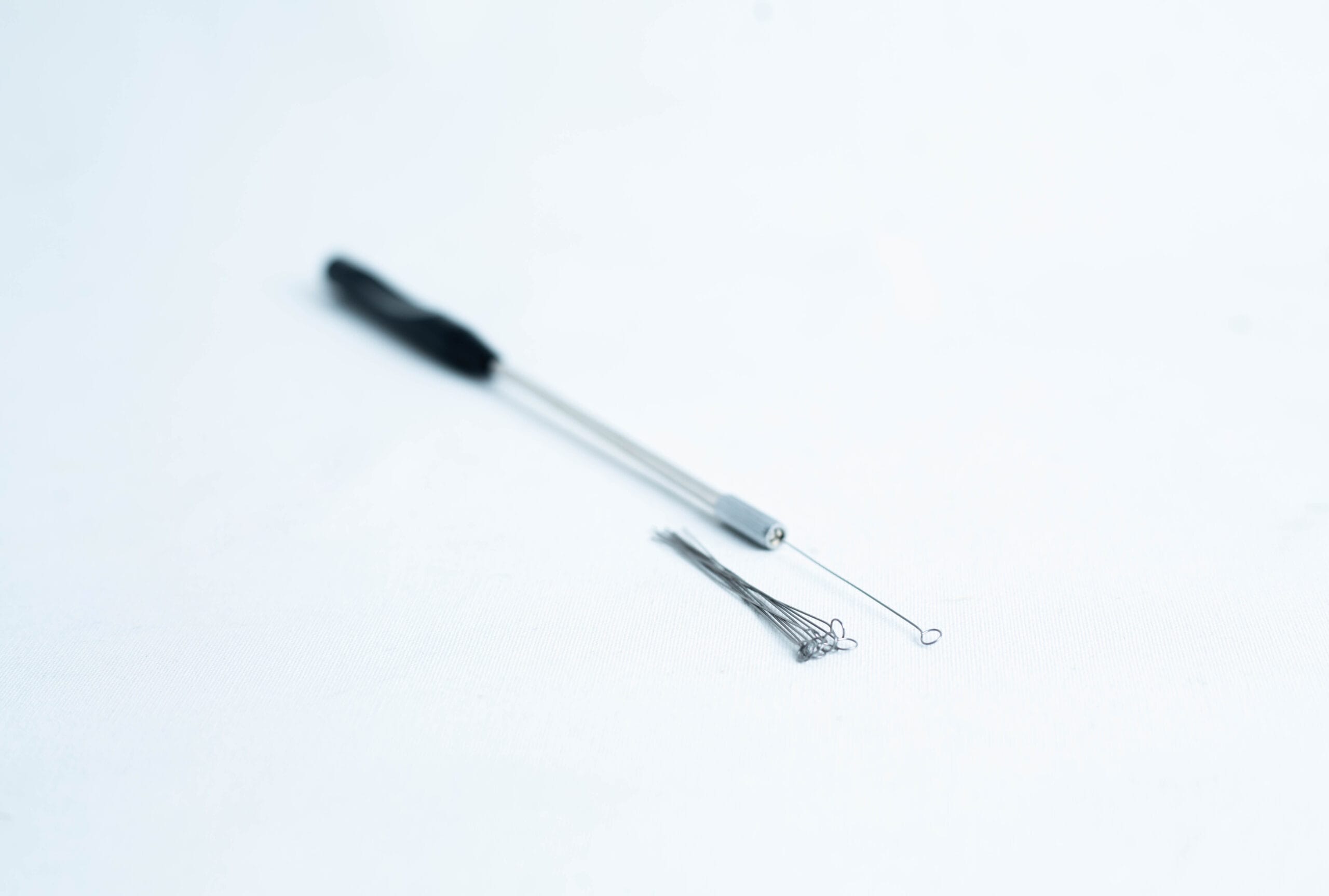 Close-up of a metal inoculating loop tool and spare loops on a white surface.