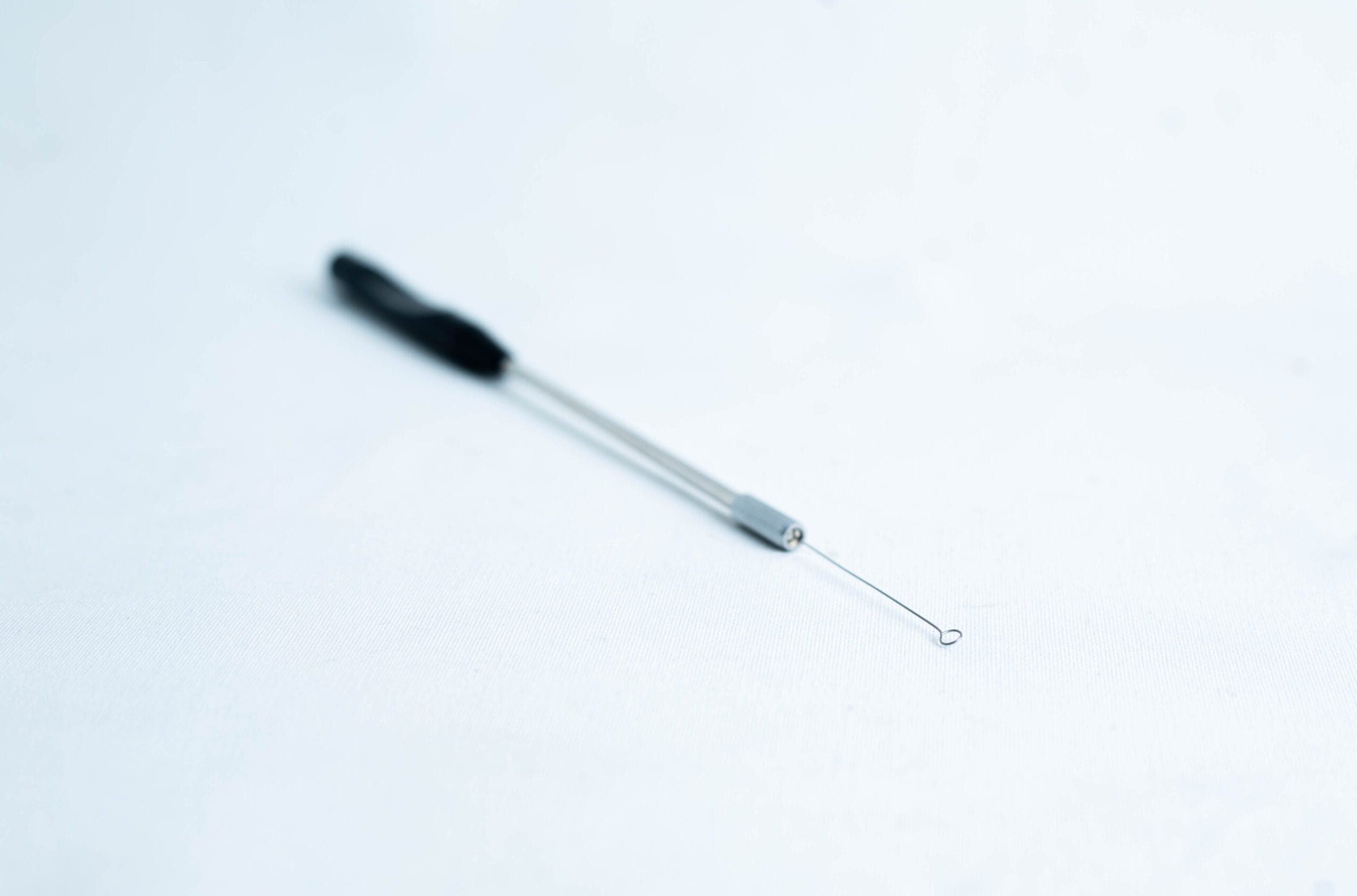 A close-up of a metal blackhead remover tool on a white surface.
