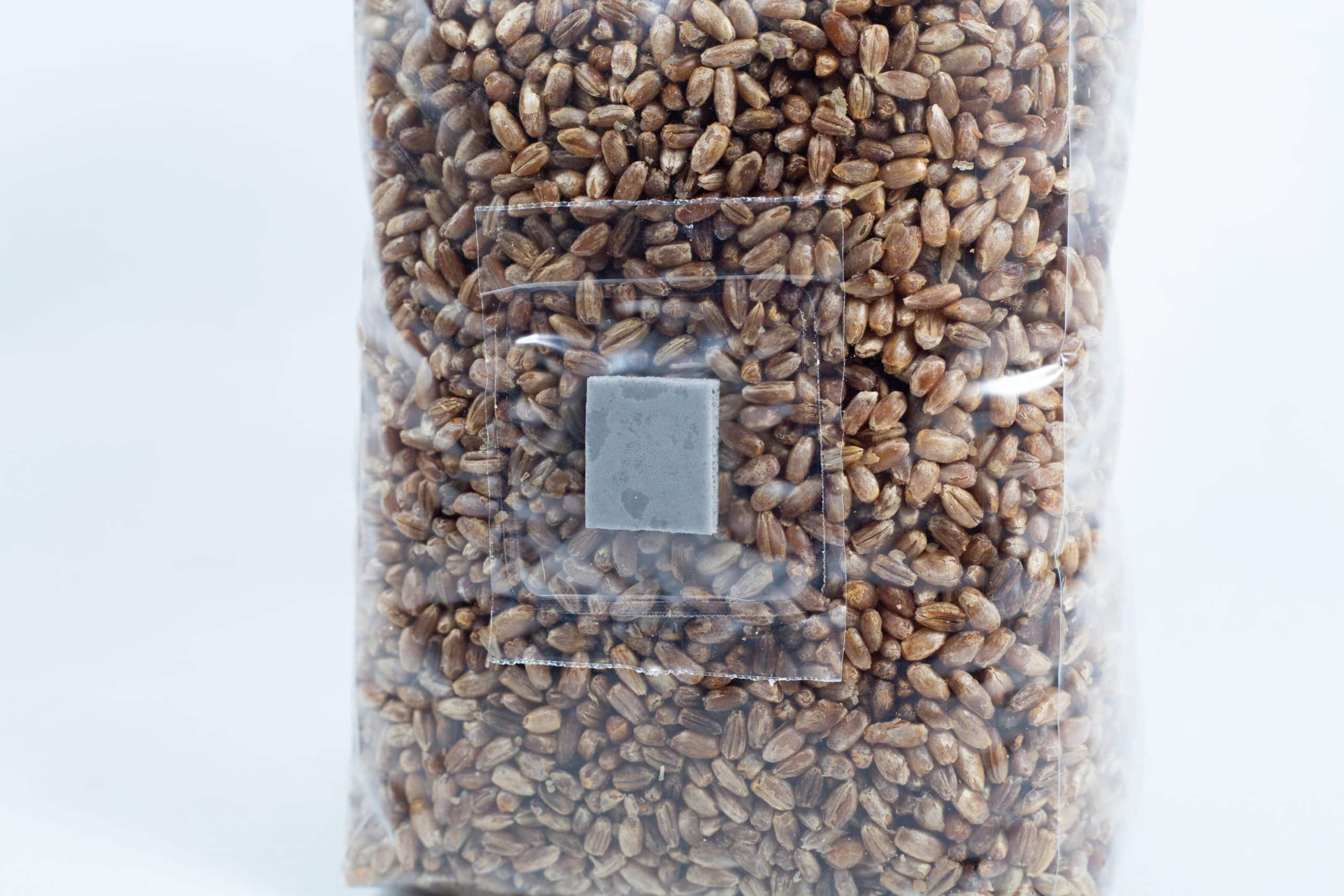 A clear plastic bag filled with pre-sterilised organic rye grain for mushroom cultivation, sealed with an injection port and air-filter patch.