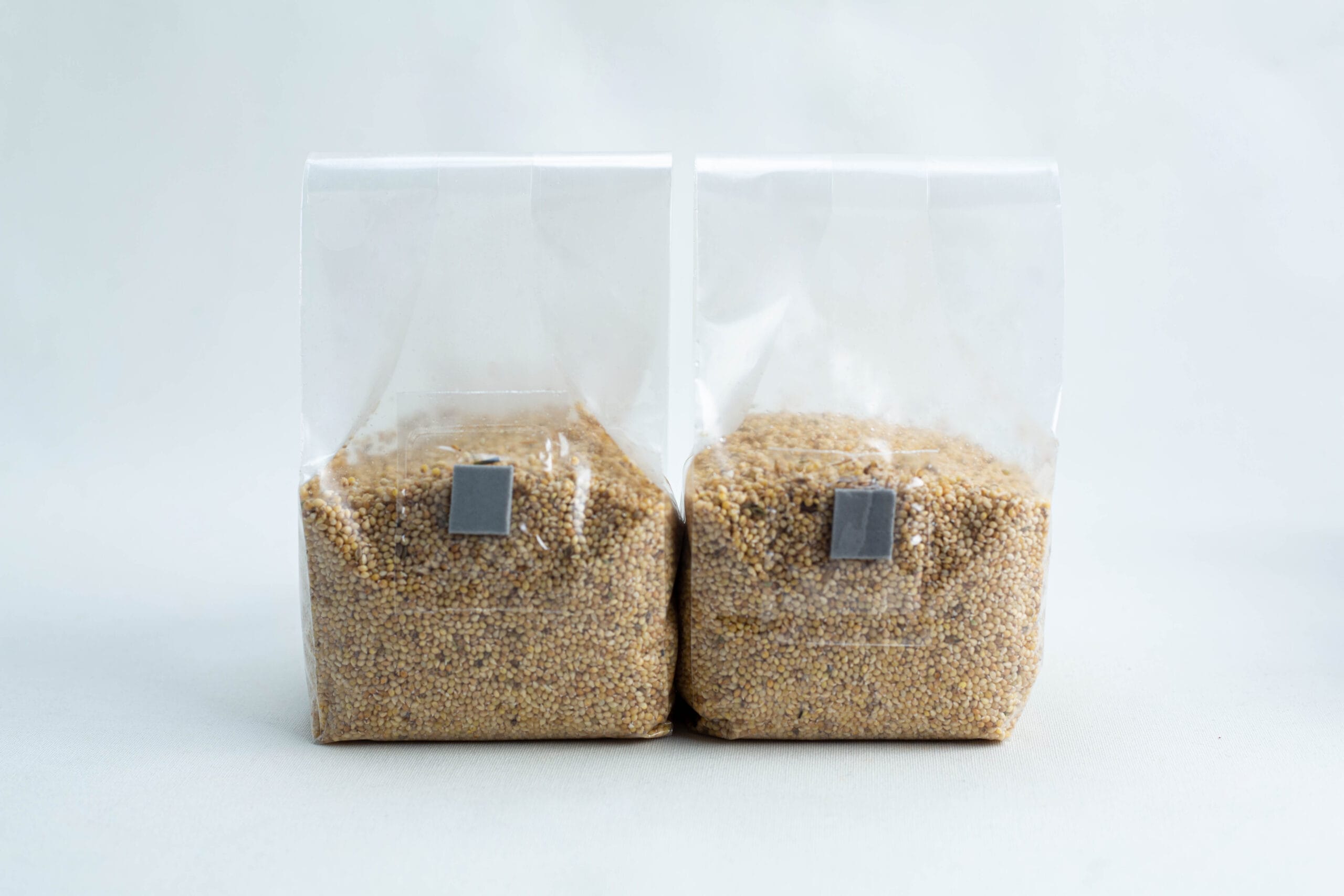 Two clear plastic bags filled with grains, standing side by side on a white background.