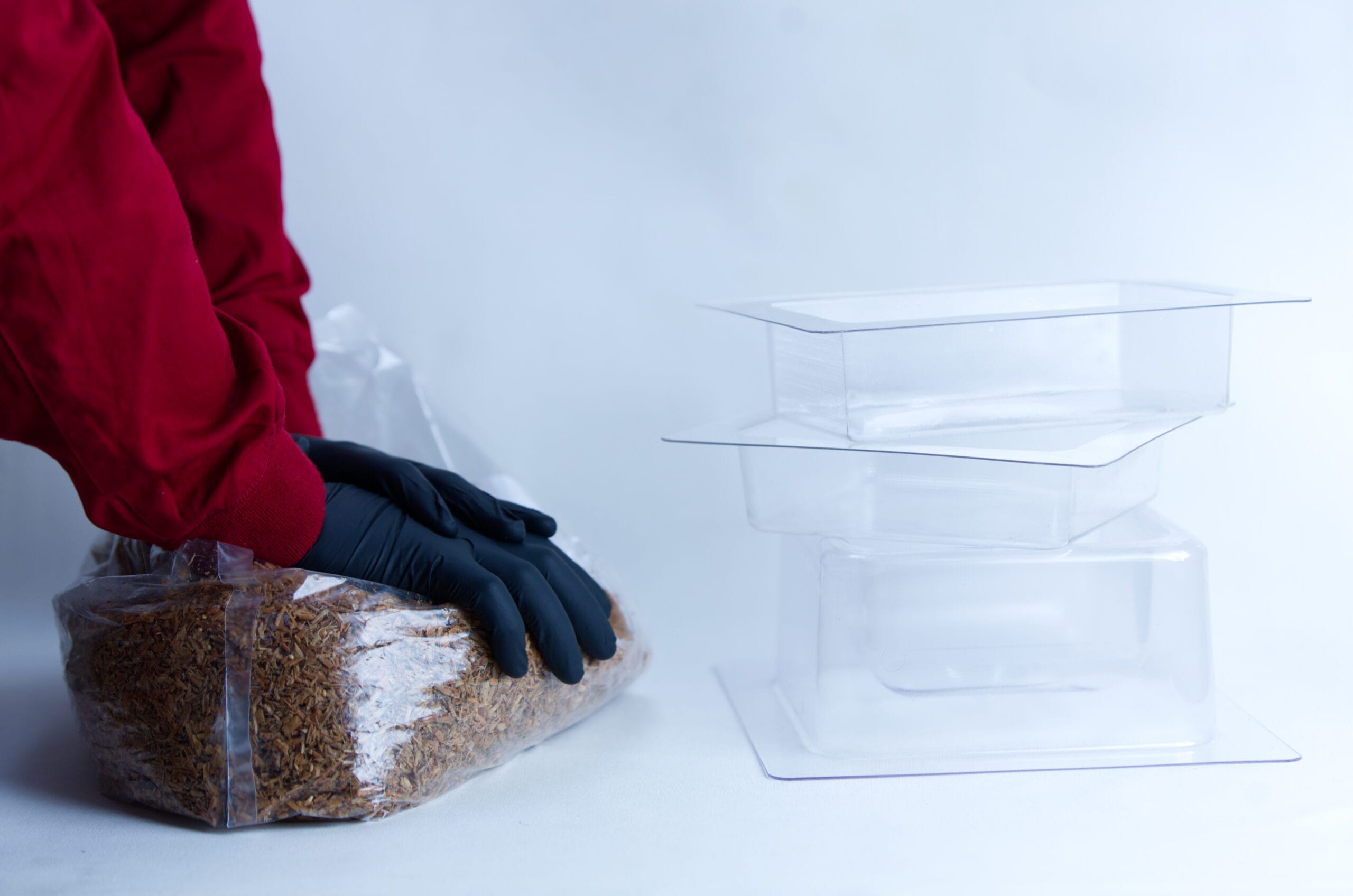 Person in red sleeves and black gloves handling a plastic bag of dried food beside empty plastic containers.