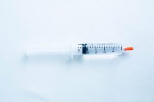 A plastic syringe with a red cap placed on a light blue surface.