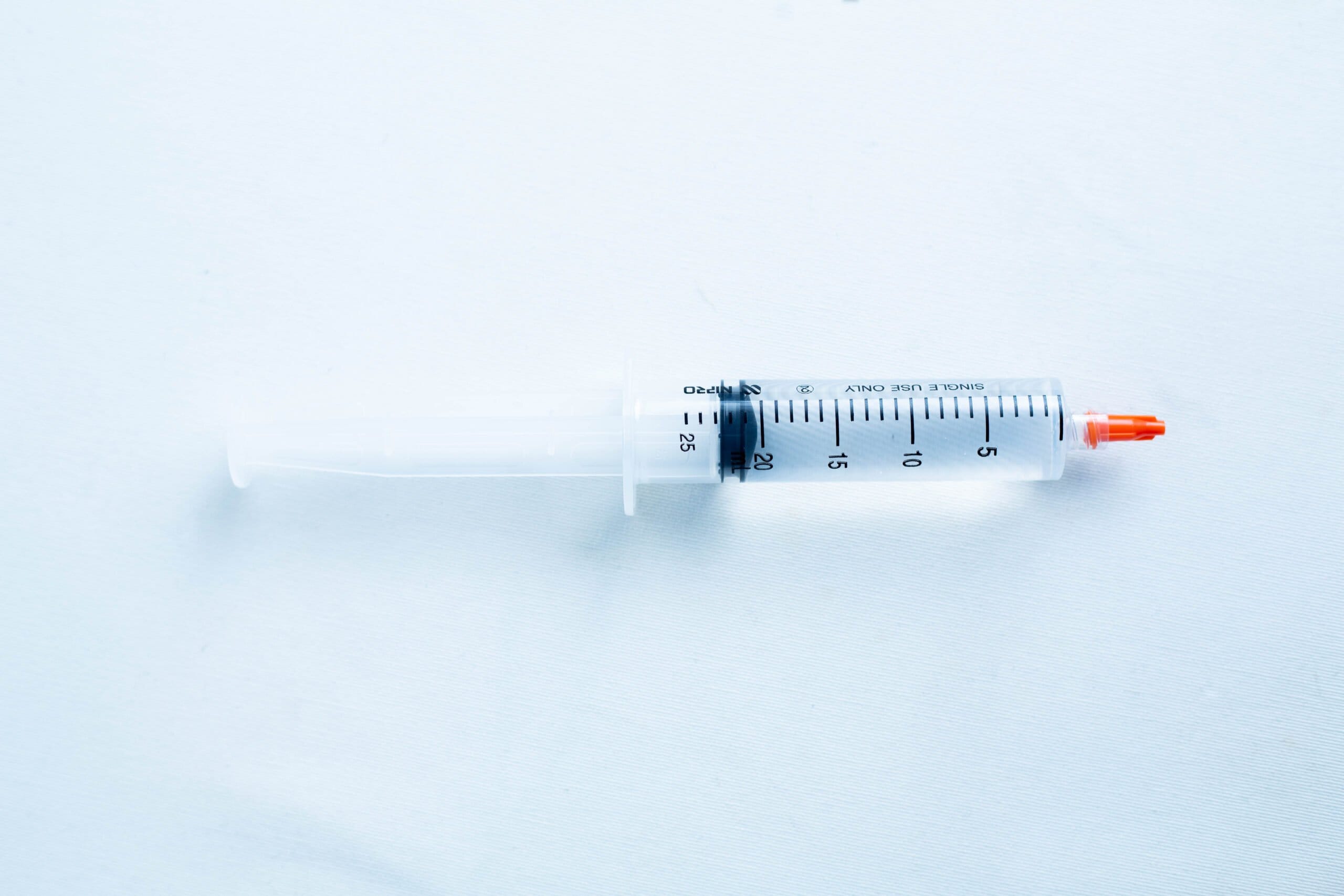 A plastic syringe with a red cap placed on a light blue surface.