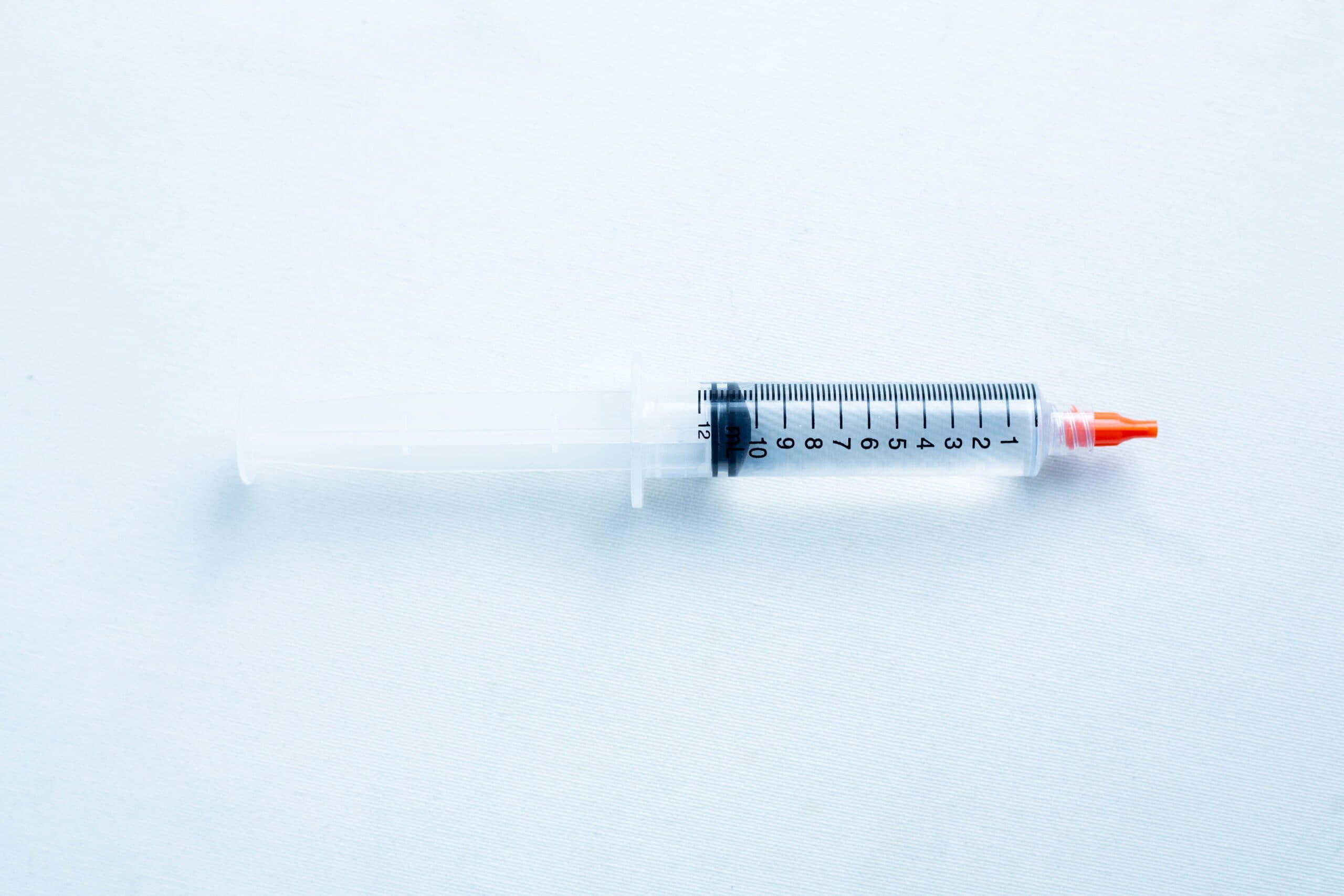 A plastic syringe with a red cap and black measurement markings lies on a white surface.