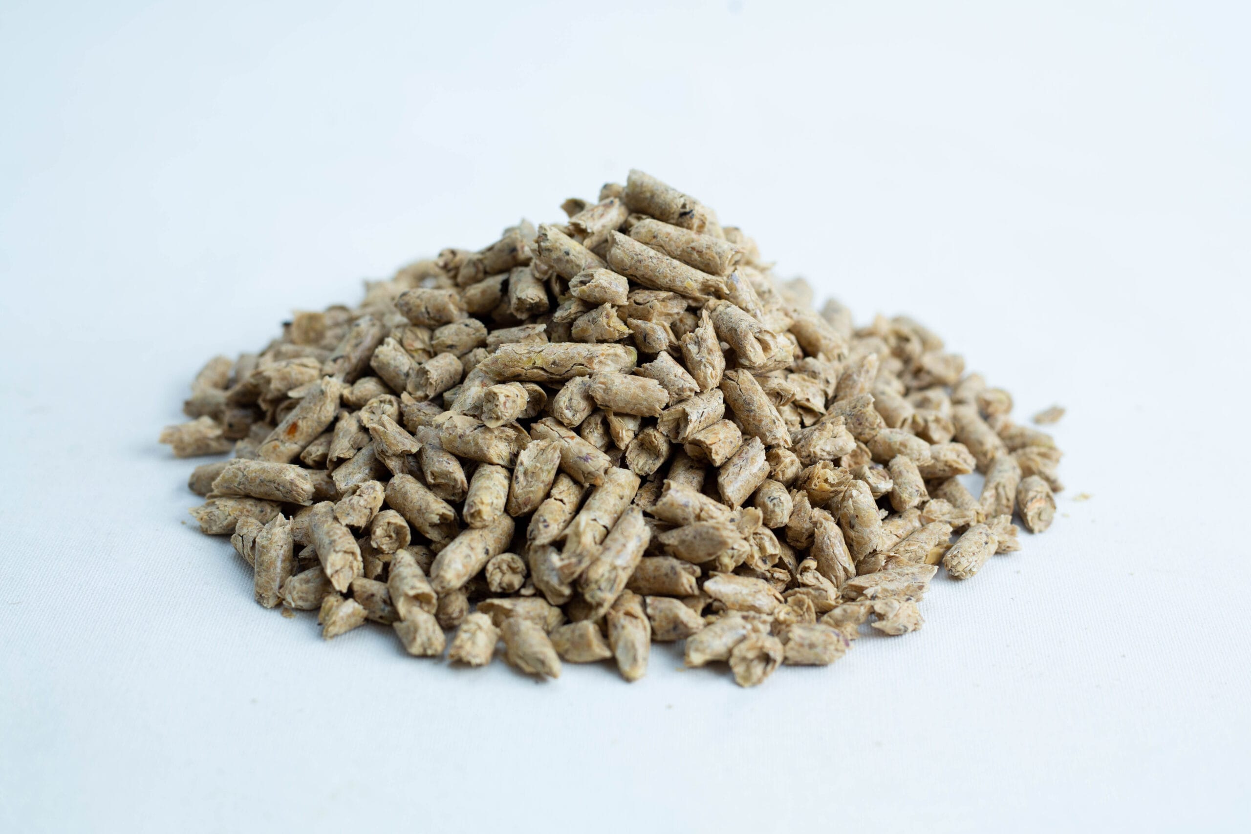 A pile of Maxisoy Soya Hull Pellets animal feed (20kg), light brown in colour, rests on a white background.