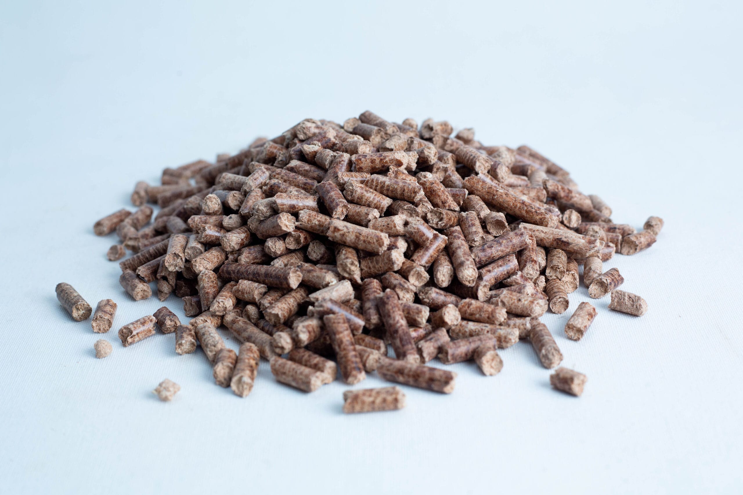 A pile of brown cylindrical wood pellets on a white surface.