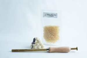 A packet of organic beeswax, wax pellets, and a wooden-handled wax sealing tool on a white background.