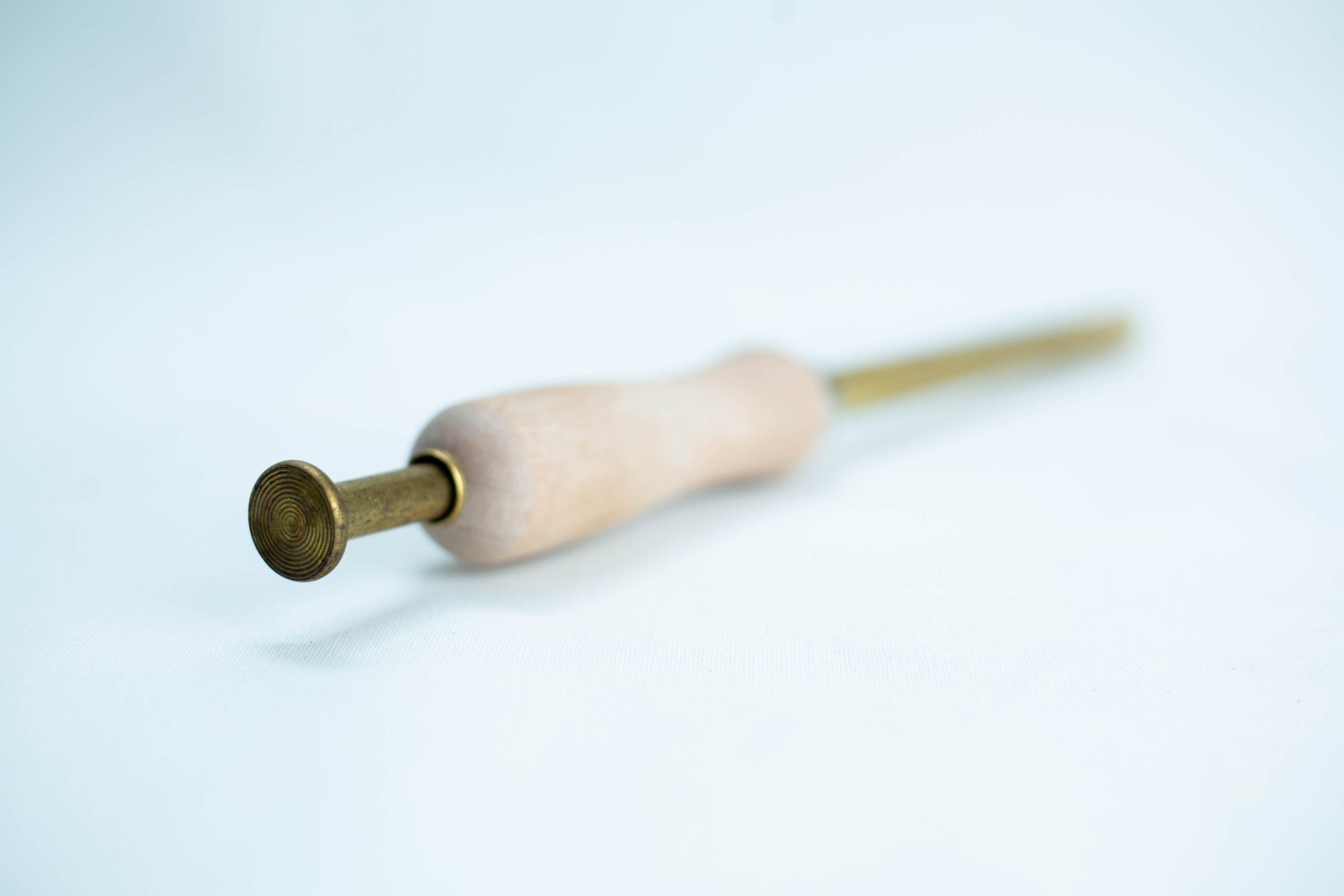 A brass and wooden tool with a round textured tip, lying on a white surface.